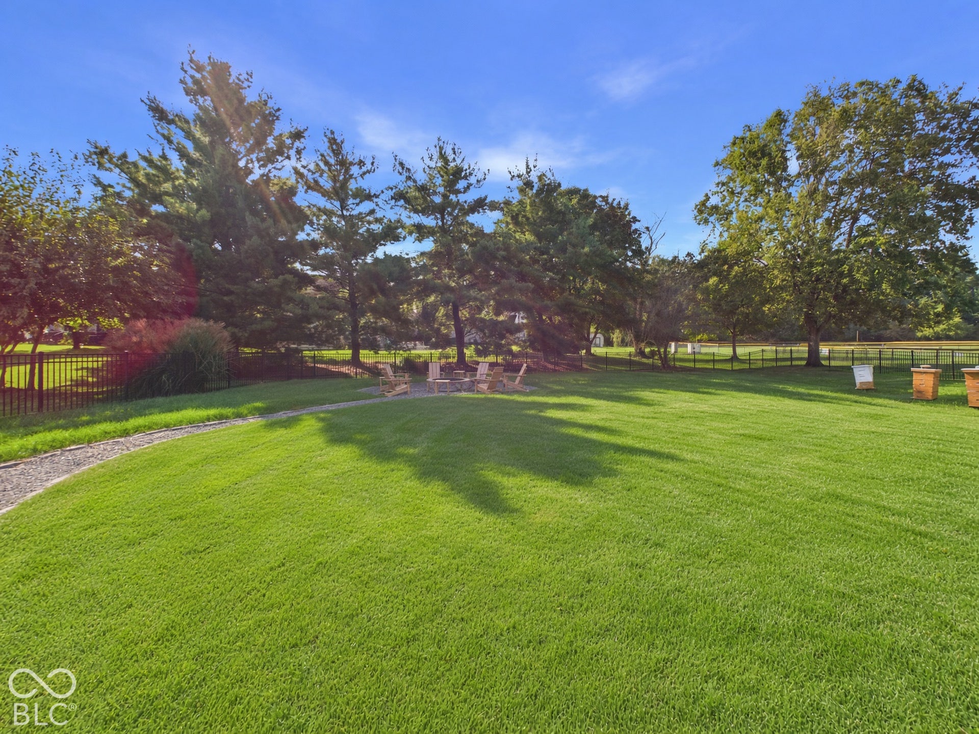 Expansive lawn with a gravel pathway, mature trees, and a black metal fence