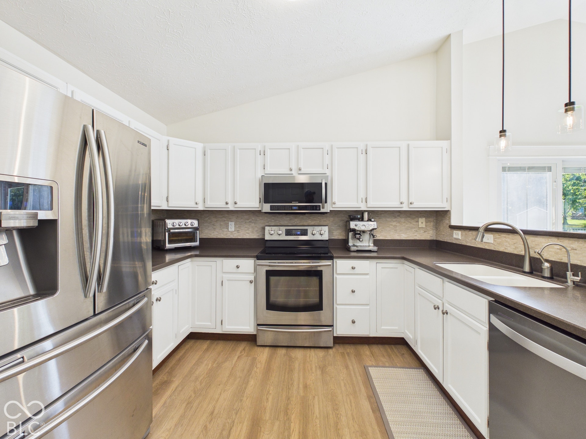 Kitchen featuring white cabinetry, stainless steel appliances, wood-finish flooring, and a vaulted ceiling