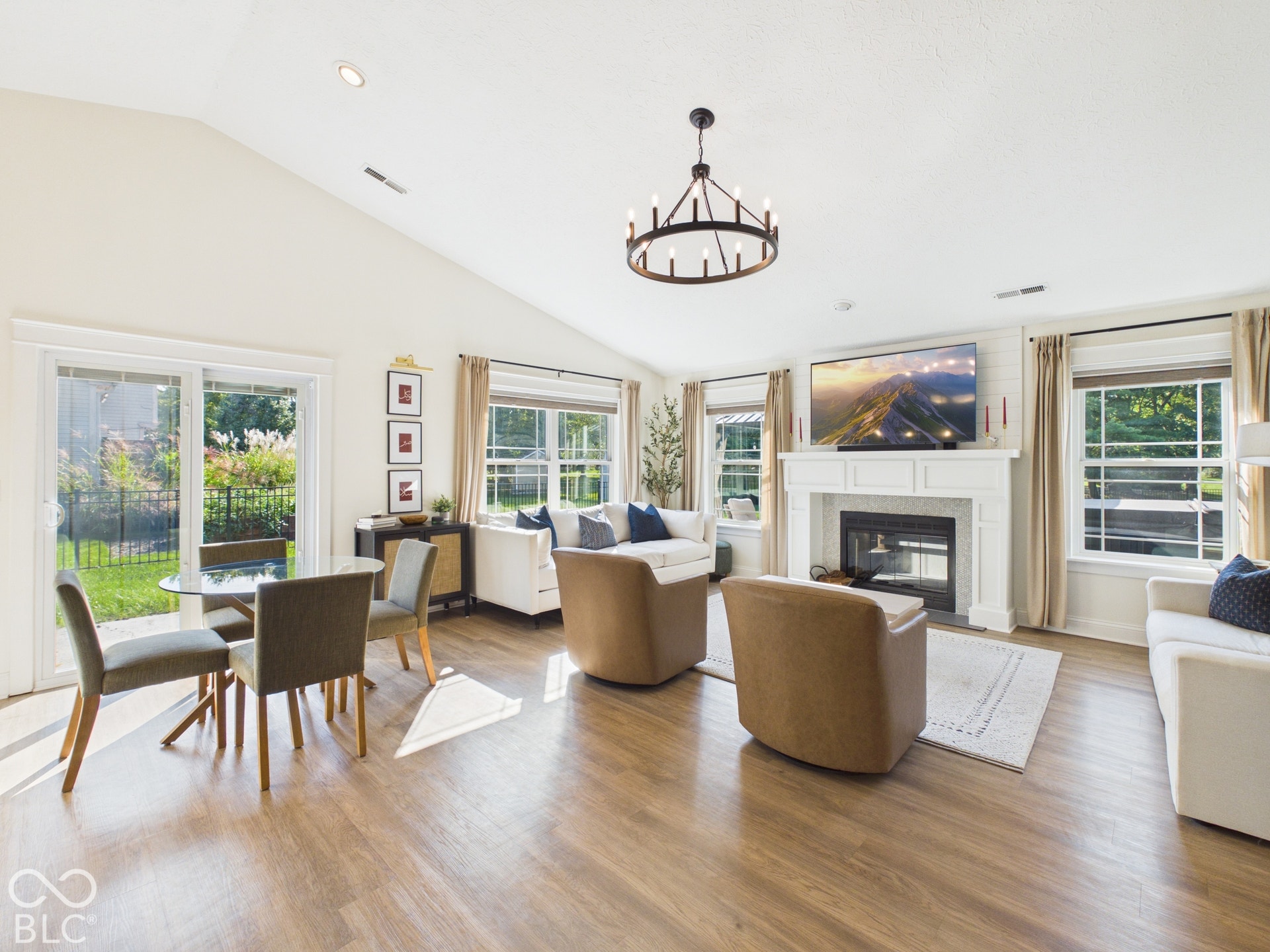 Vaulted ceiling, wood-finish flooring, fireplace with white mantel, sliding glass door, and multiple windows