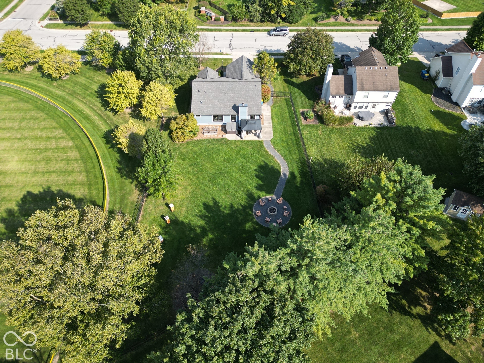 Expansive backyard featuring a manicured lawn, mature trees, a circular paver patio with a built-in fire pit, and a curved stone pathway