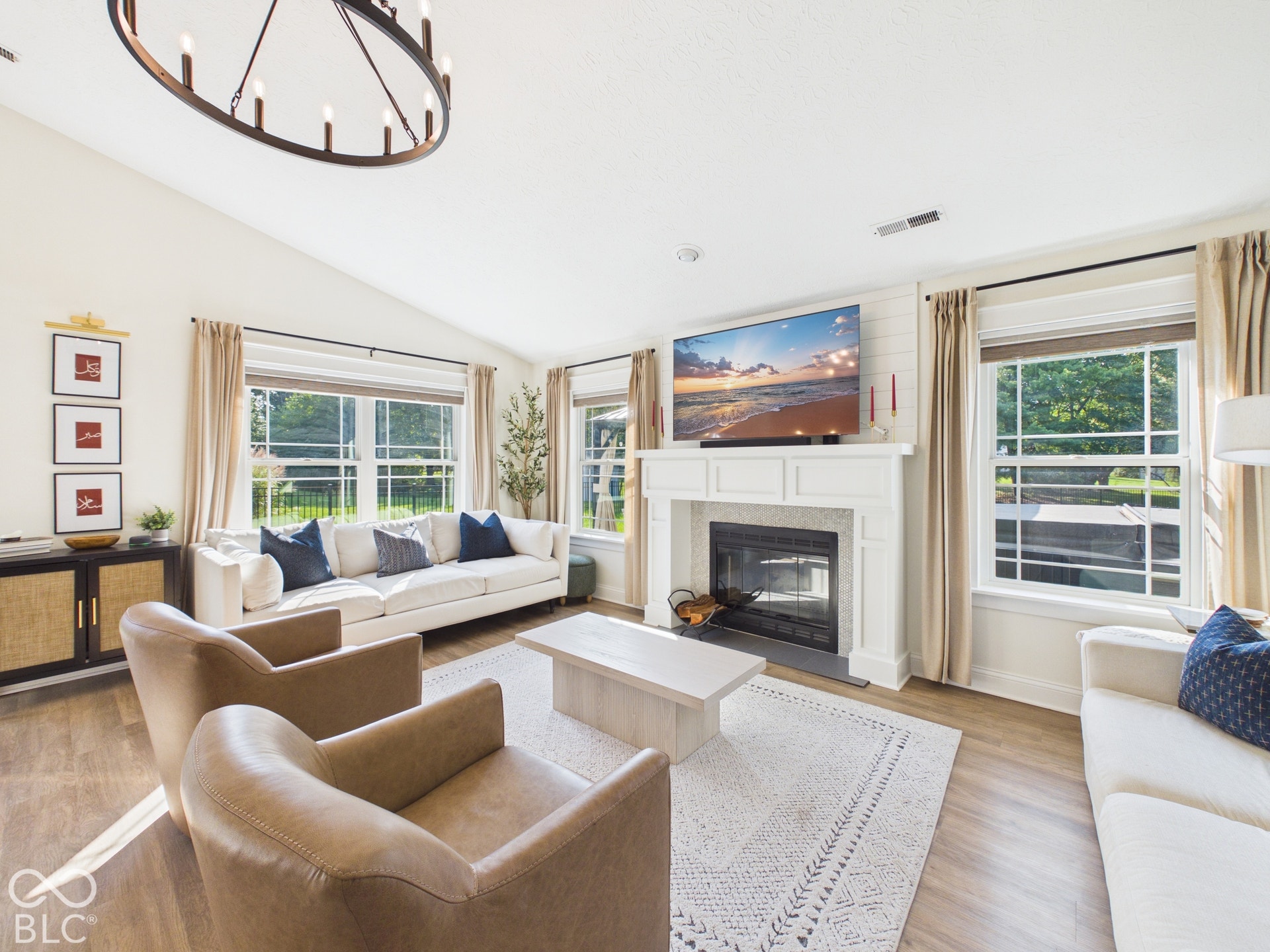 Vaulted ceiling with an oval chandelier, wood-finish flooring, white fireplace with shiplap accent wall, and multiple double-hung windows