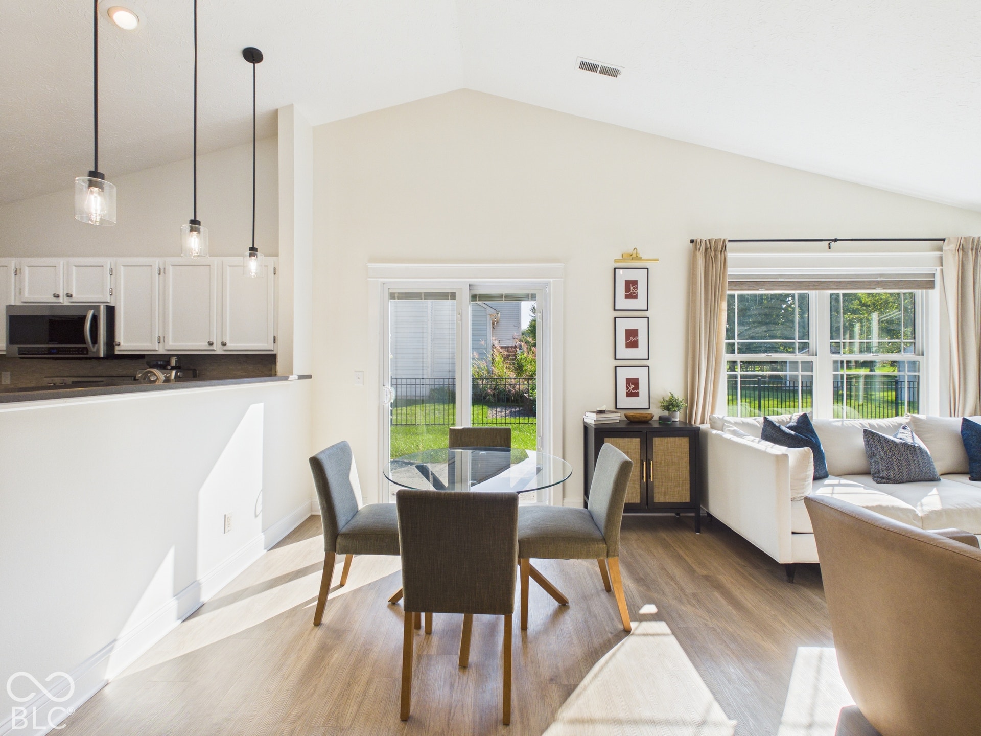 Vaulted ceiling, wood-finish flooring, white cabinetry, dark countertops, and sliding glass door