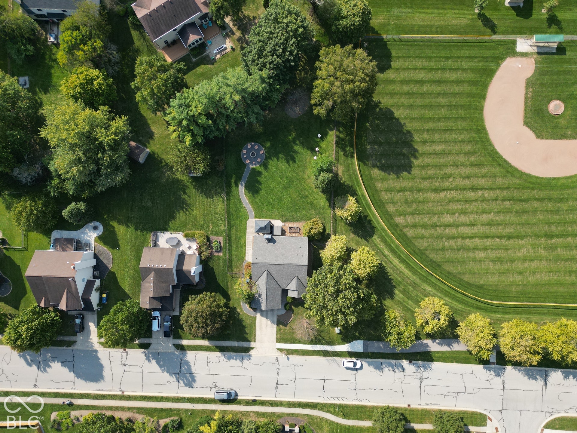 Aerial perspective featuring a residential street, a neighboring baseball field, and multiple homes with private yards
