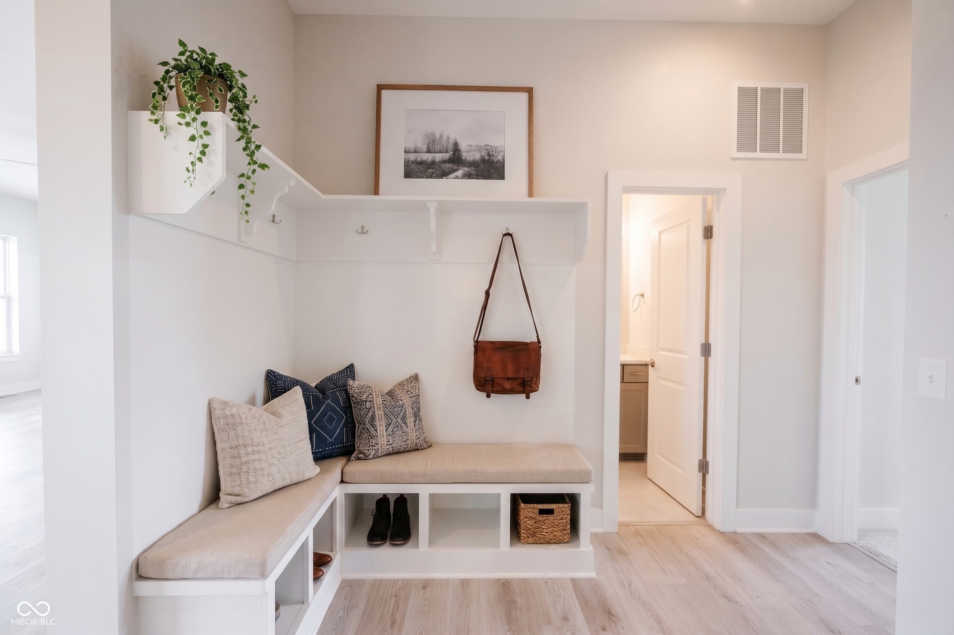 Built-in bench seating with cubby storage, integrated shelving, coat hooks, and laminated wood-finish flooring.  This photo has been virtually stage.