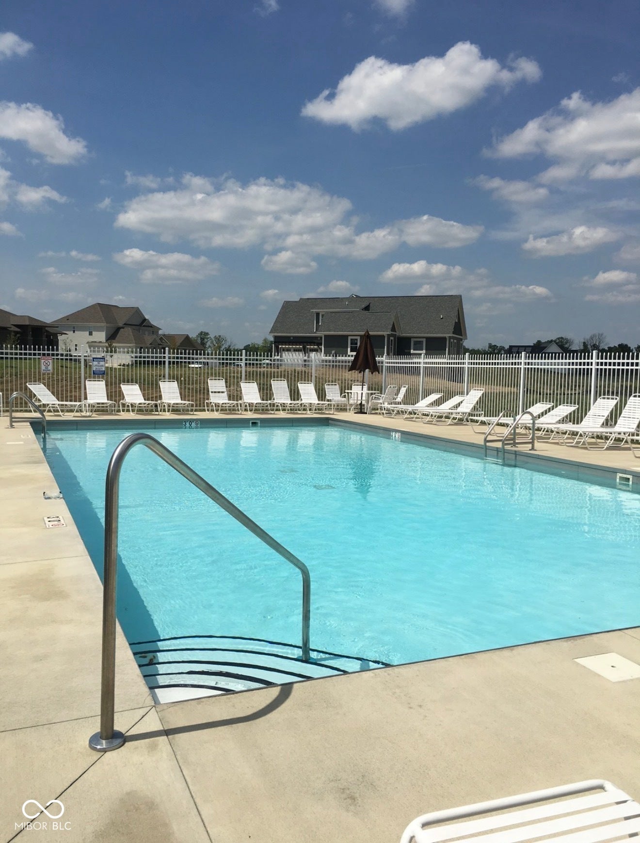 Rectangular swimming pool with integrated steps, surrounded by a concrete deck and fencing