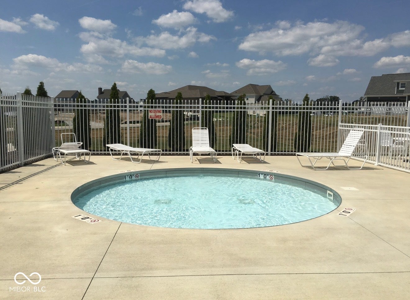 Circular in-ground pool with surrounding concrete decking, enclosed by a white metal fence