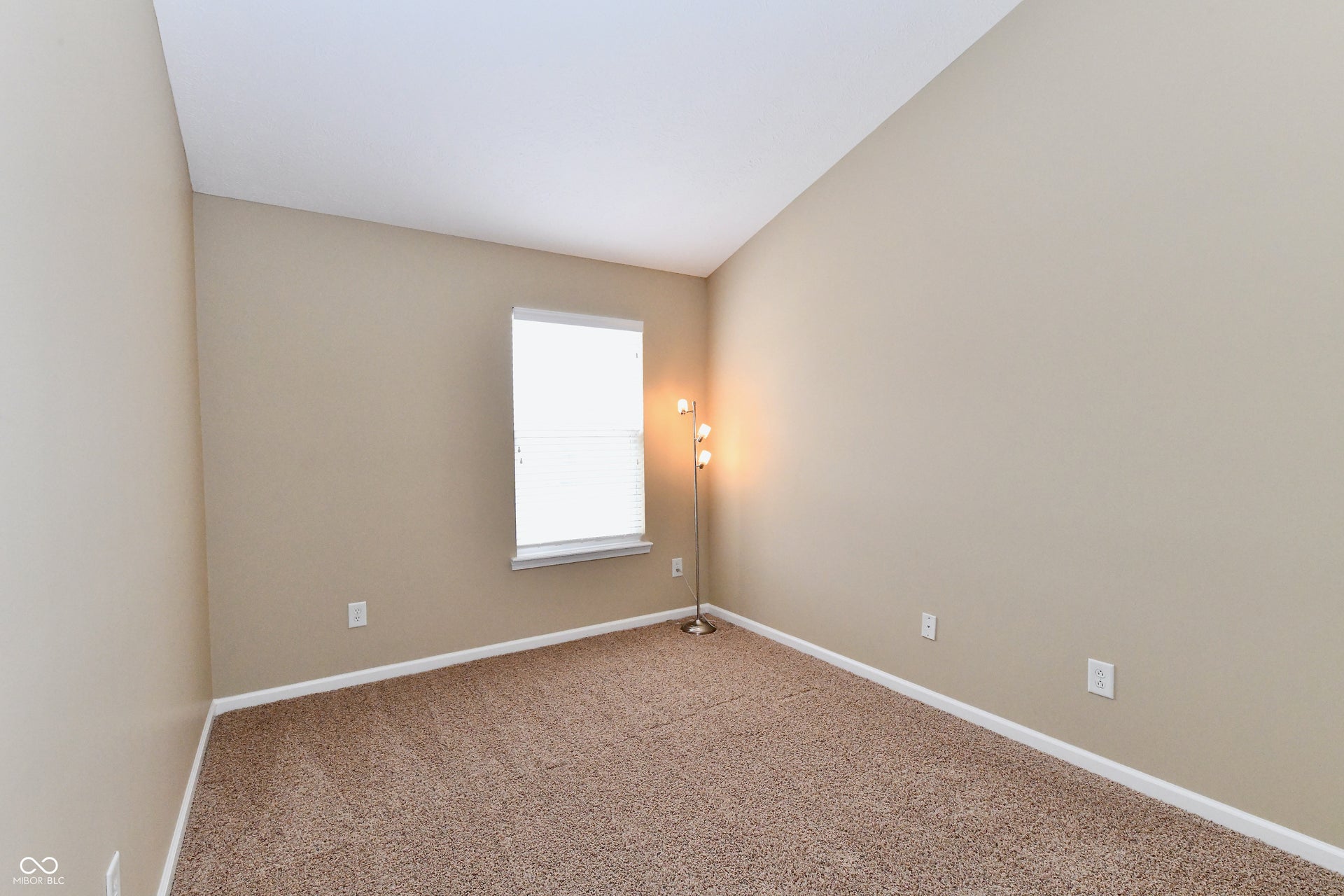 Carpeted flooring, vaulted ceiling, neutral wall tones, and a window with blinds