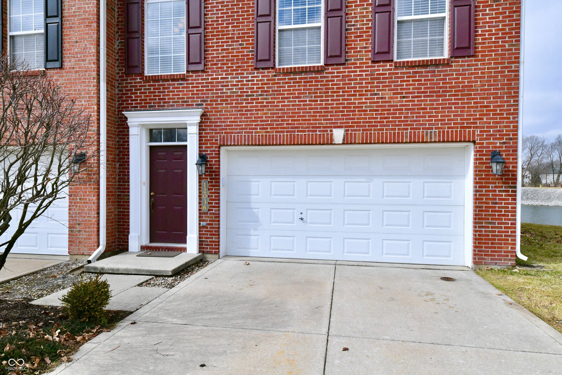 Brick exterior with white garage doors, decorative shutters, and an ornate entry surround