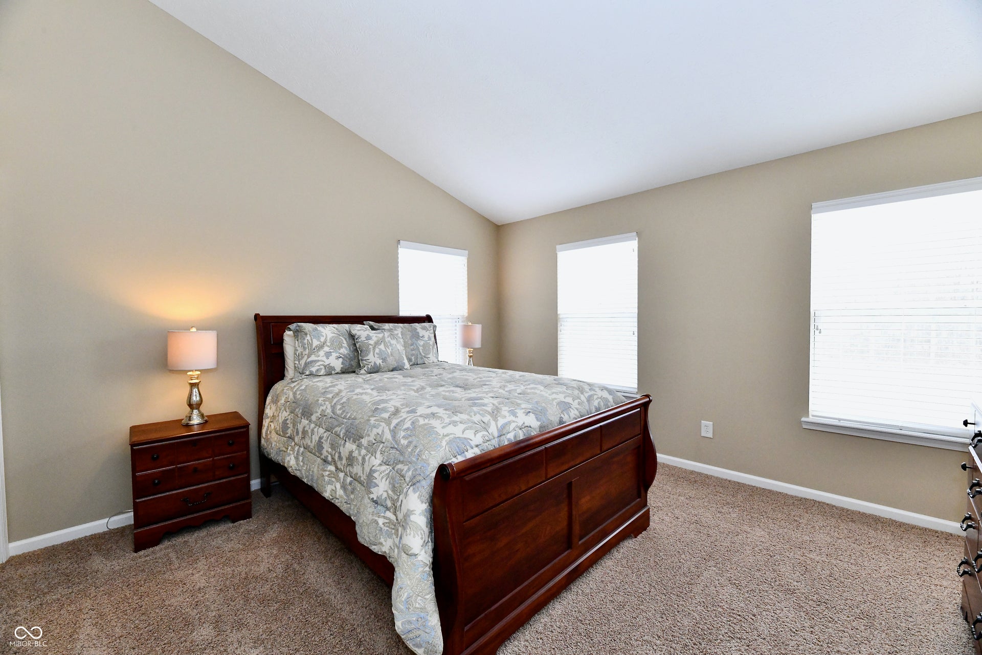 Vaulted ceiling, neutral wall paint, two windows with blinds, and carpeted flooring