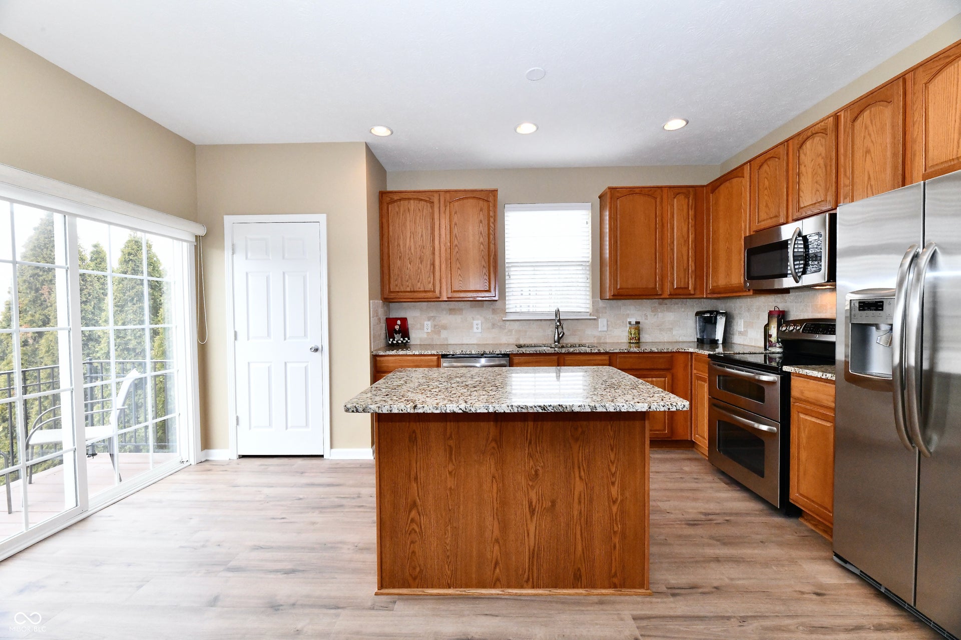 Kitchen featuring wood-finish flooring, recessed lighting, wood cabinetry, stainless steel appliances, and a central island with a stone countertop