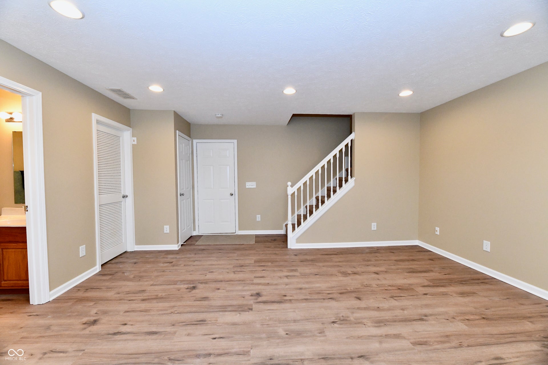 Wood-finish flooring throughout, recessed ceiling lighting, a white painted staircase with wood treads, and neutral wall tones