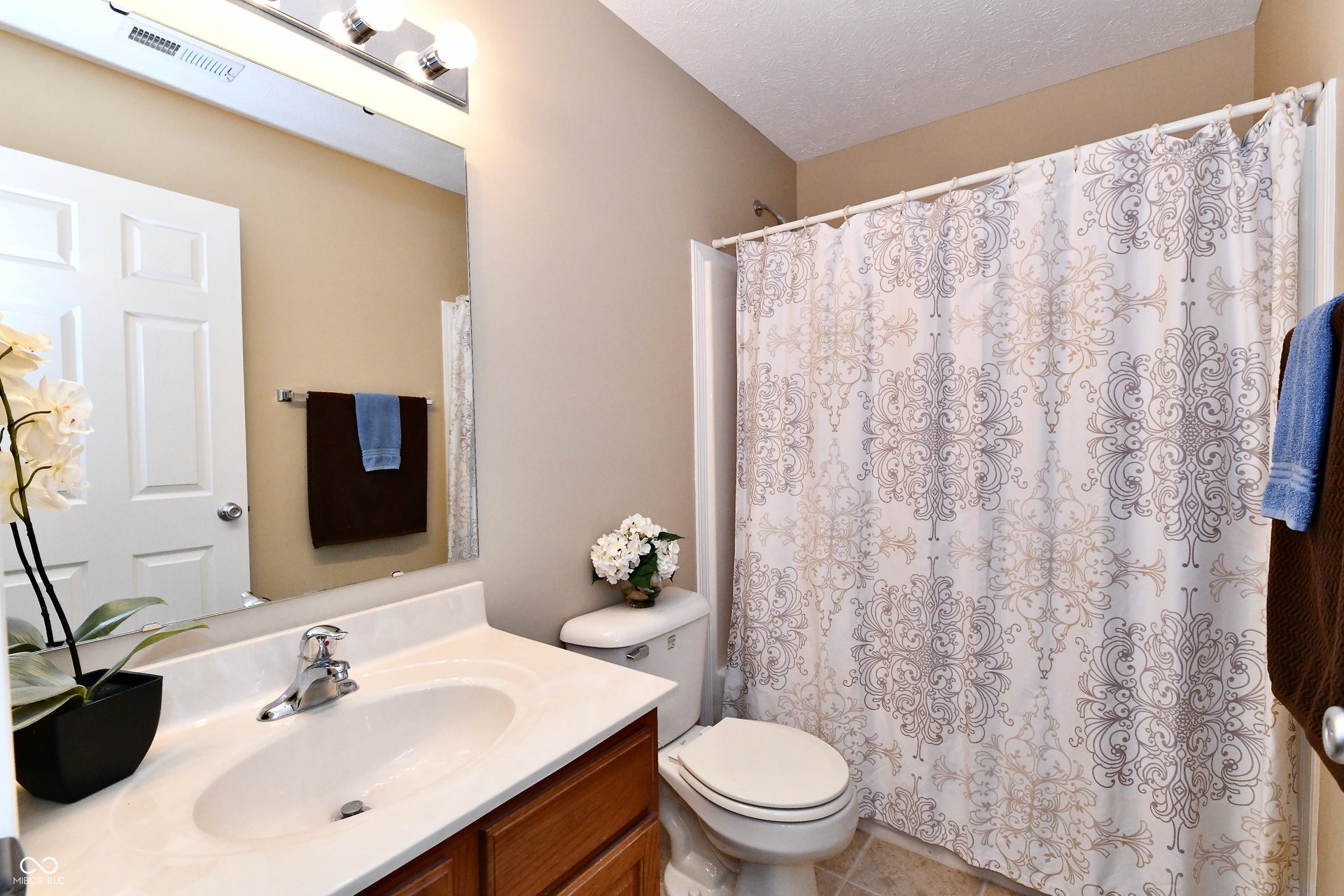 Bathroom featuring a vanity with a white countertop and built-in sink, a wall-mounted mirror with lighting, and a shower with a shower curtain
