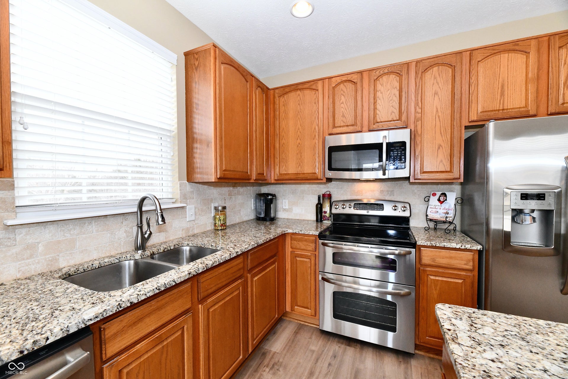 Well-appointed kitchen featuring wood cabinetry, granite countertops, stainless steel appliances, a tile backsplash, and a double basin sink