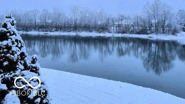 Waterfront setting with a snow-covered bank and mature trees