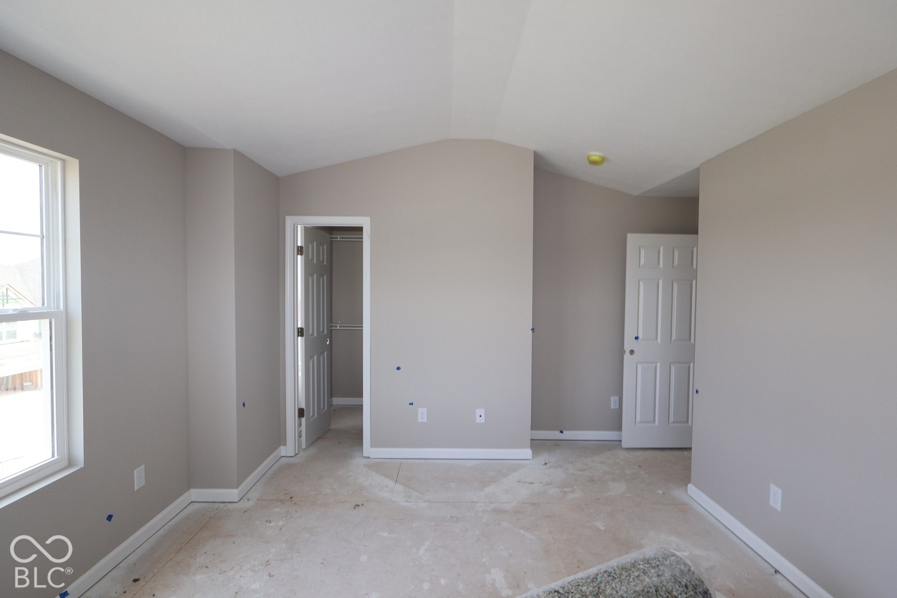 Vaulted ceiling, neutral wall paint, white trim, paneled interior doors, and a window