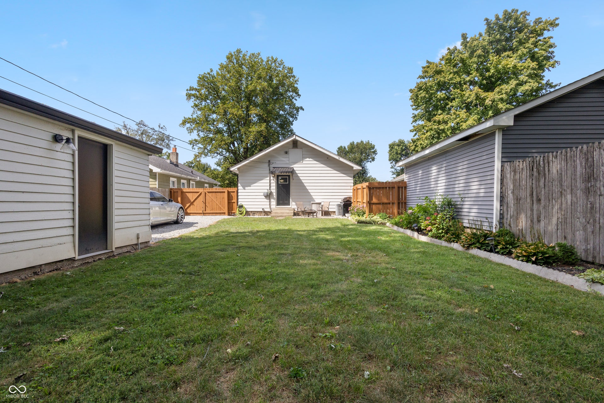 4927 Caroline Avenue, Indianapolis, IN 46205 Expansive green lawn with mature perimeter trees, bordered by a privacy fence, and featuring an outbuilding with siding