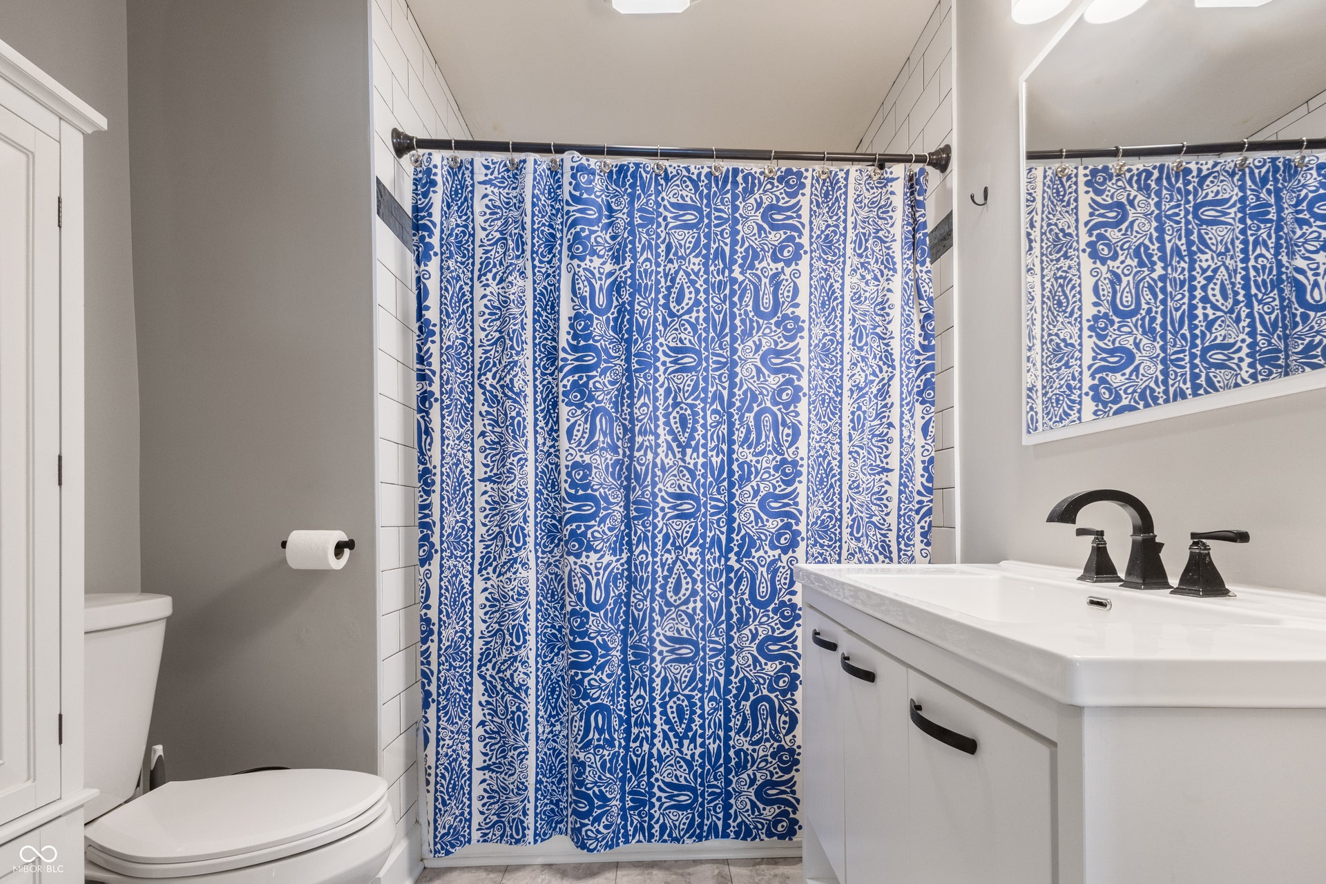 4927 Caroline Avenue, Indianapolis, IN 46205 White subway tile shower surround with an accent band, white vanity with integrated sink, matte black faucet, and a large wall-mounted mirror