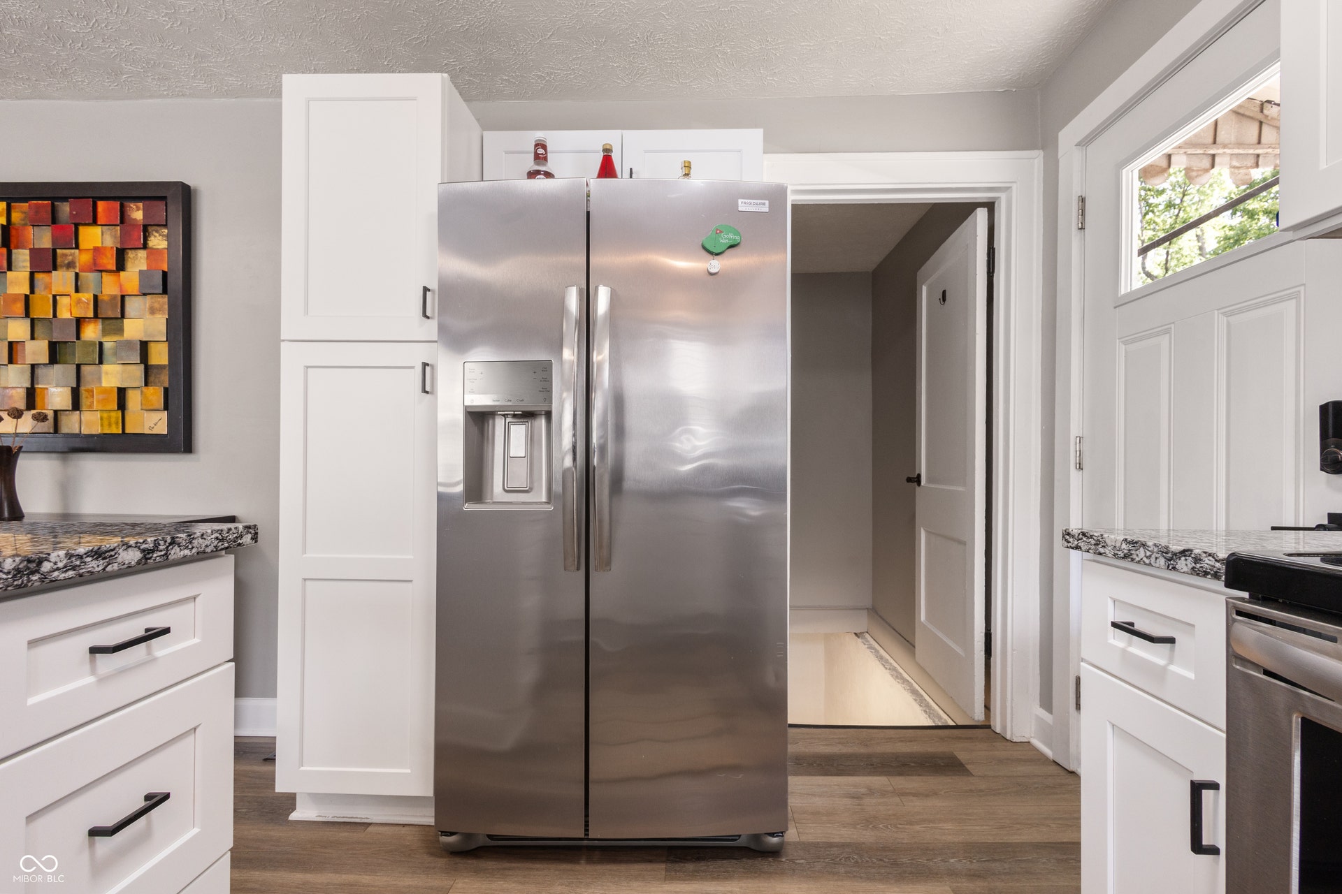4927 Caroline Avenue, Indianapolis, IN 46205 Stainless steel side-by-side refrigerator, white shaker-style cabinetry, dark speckled countertops, wood-finish flooring, and a paneled entry door