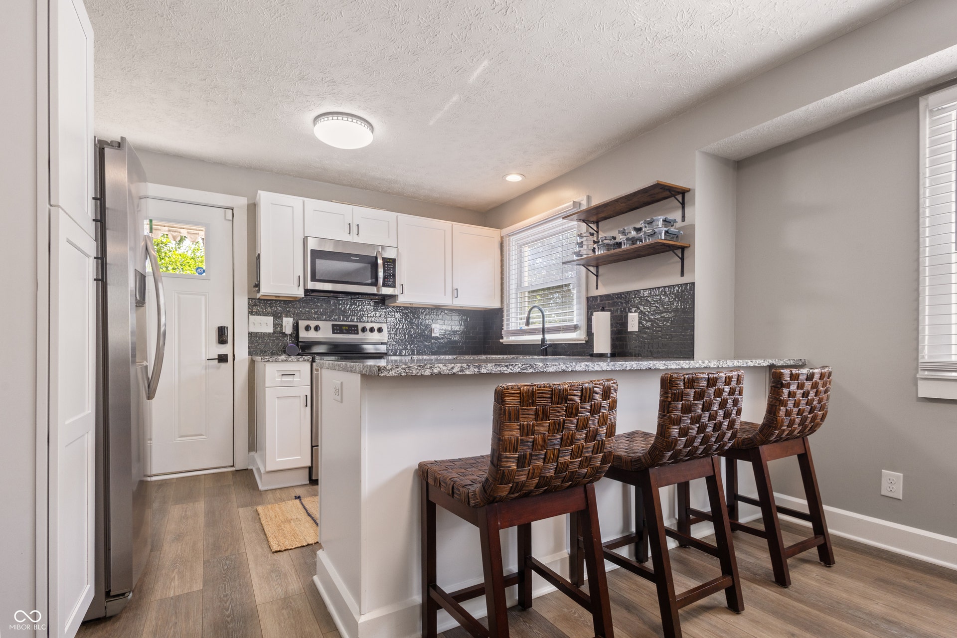 4927 Caroline Avenue, Indianapolis, IN 46205 Fully updated kitchen featuring white cabinetry, stainless steel appliances, a dark tile backsplash, a breakfast bar with a stone countertop, and wood-finish flooring
