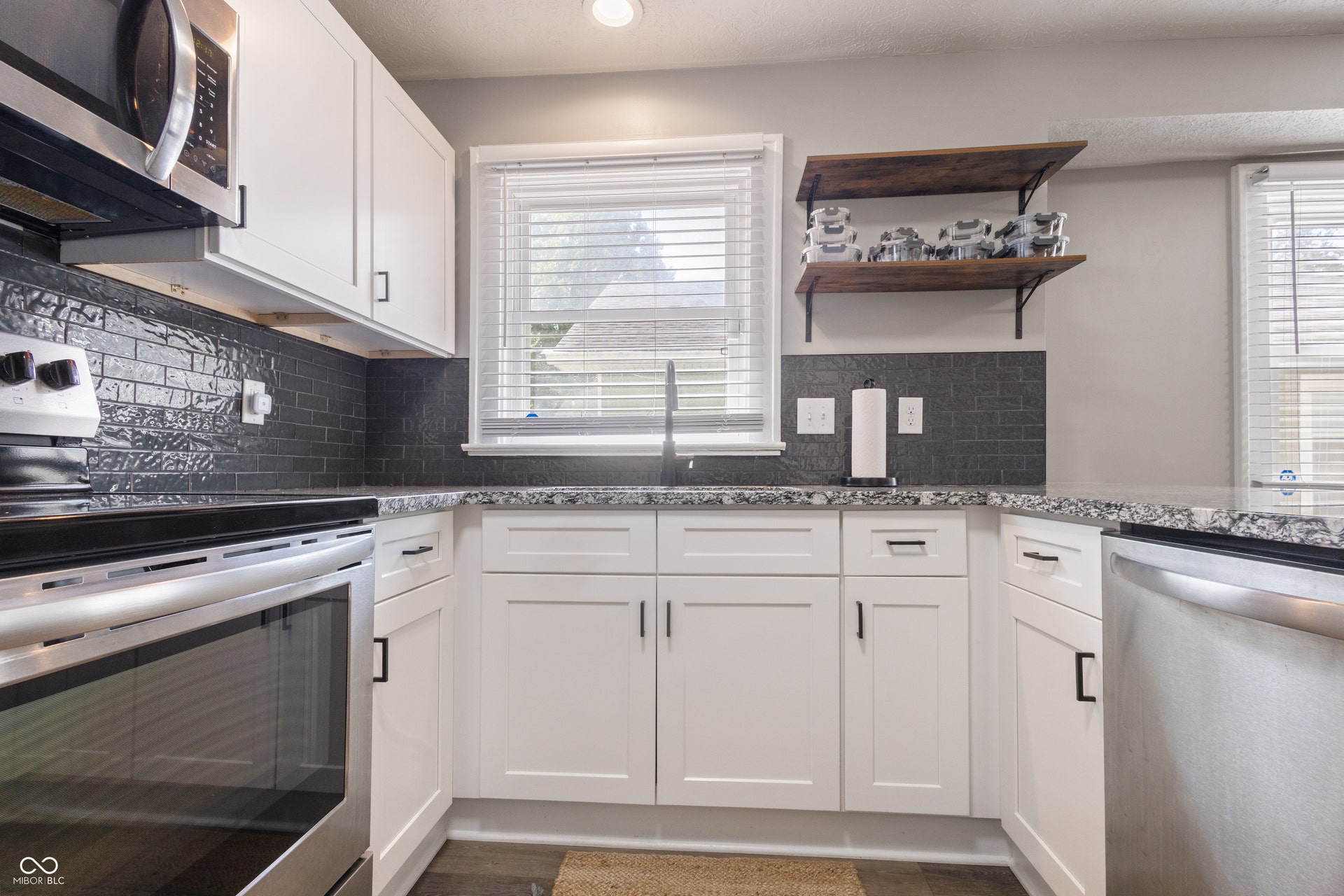 4927 Caroline Avenue, Indianapolis, IN 46205 White shaker-style cabinetry, dark subway tile backsplash, stainless steel appliances, speckled countertops, and wood-finish flooring