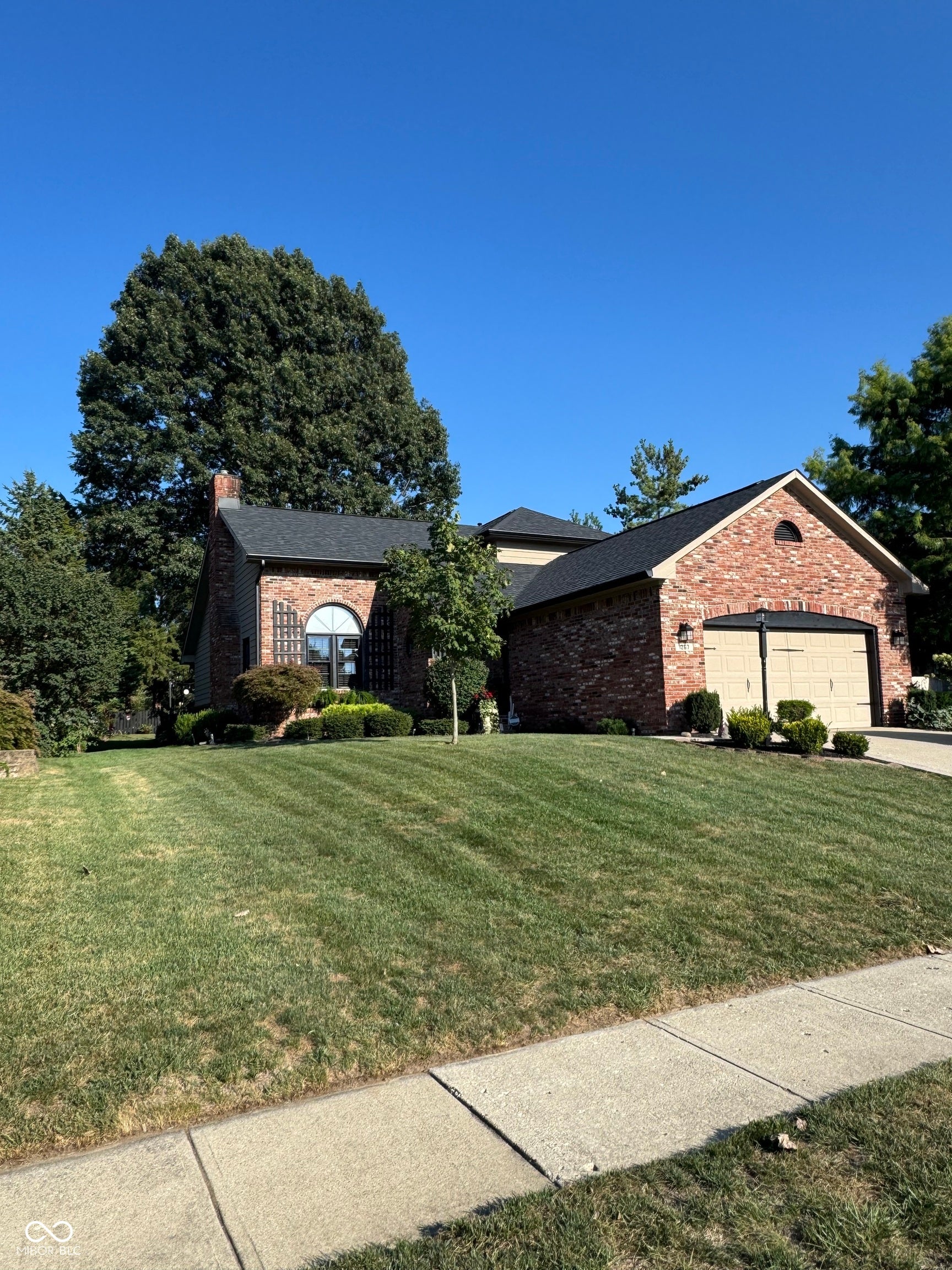 Brick exterior, arched window, attached garage, gabled roofline, and established landscaping