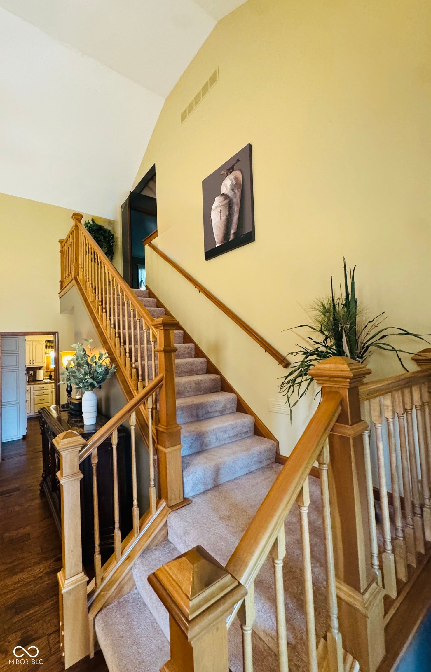 Vaulted ceiling, wood-finish railing and balusters, carpeted staircase, and wood-finish flooring