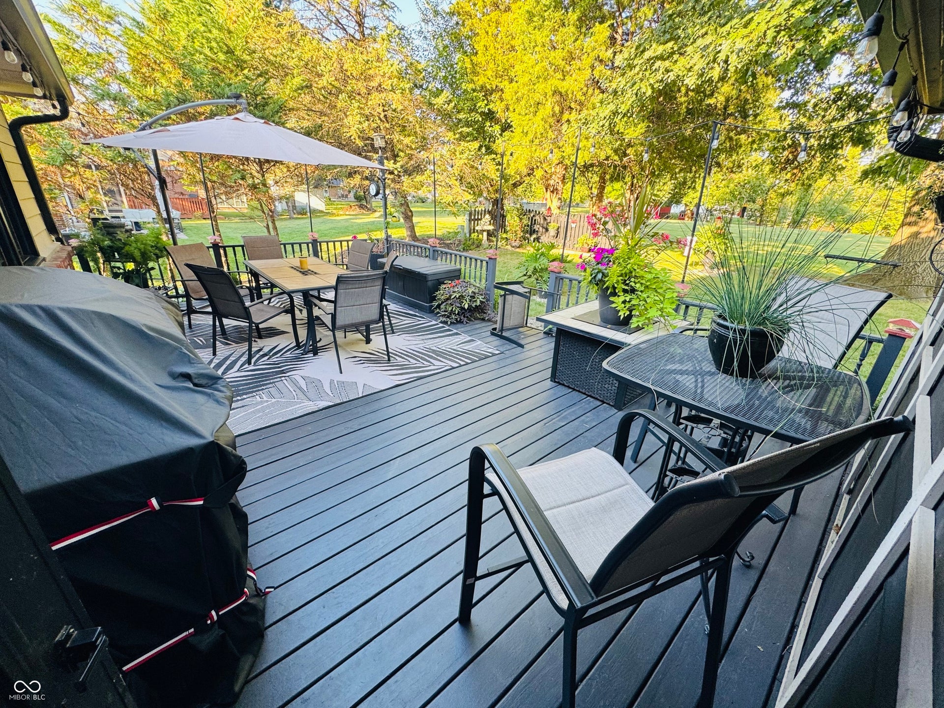 Expansive wooden deck with a dark finish, featuring dark railings and lush perimeter trees