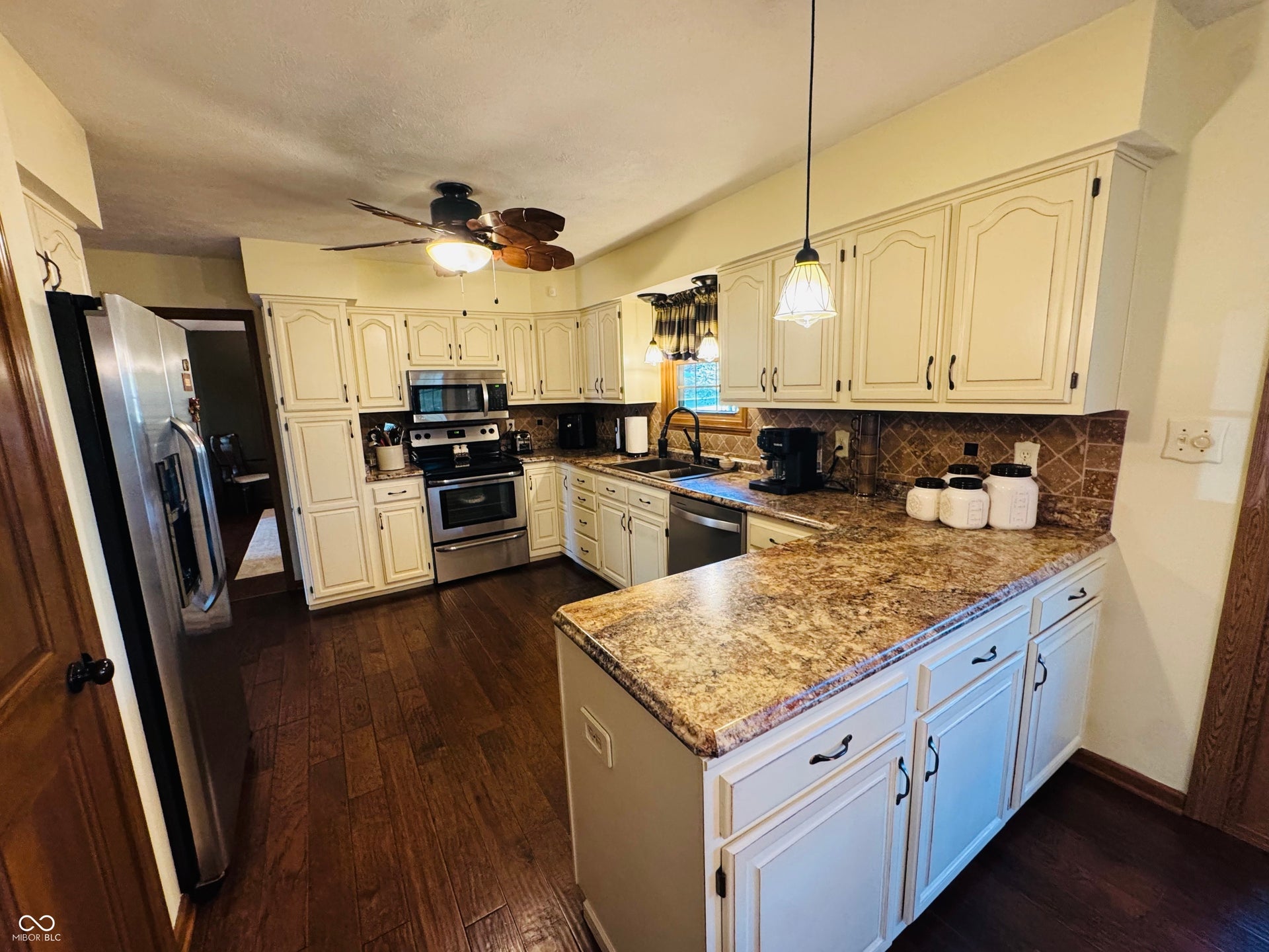 Kitchen featuring wood-finish flooring, light-toned cabinetry, stainless steel appliances, a tiled backsplash, and granite-patterned countertops