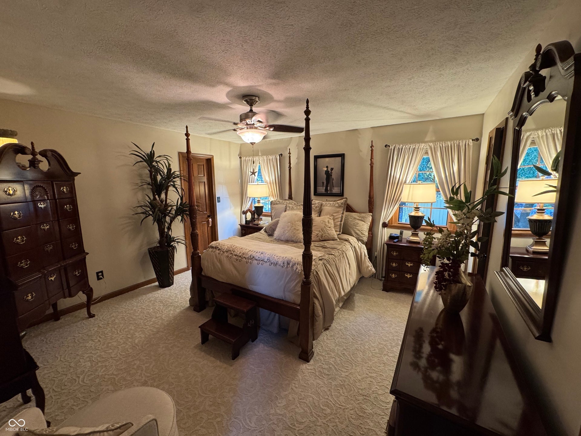 Wall-to-wall patterned carpeting, recessed window with drapes, ceiling fan with integrated lighting, and a wood-paneled door