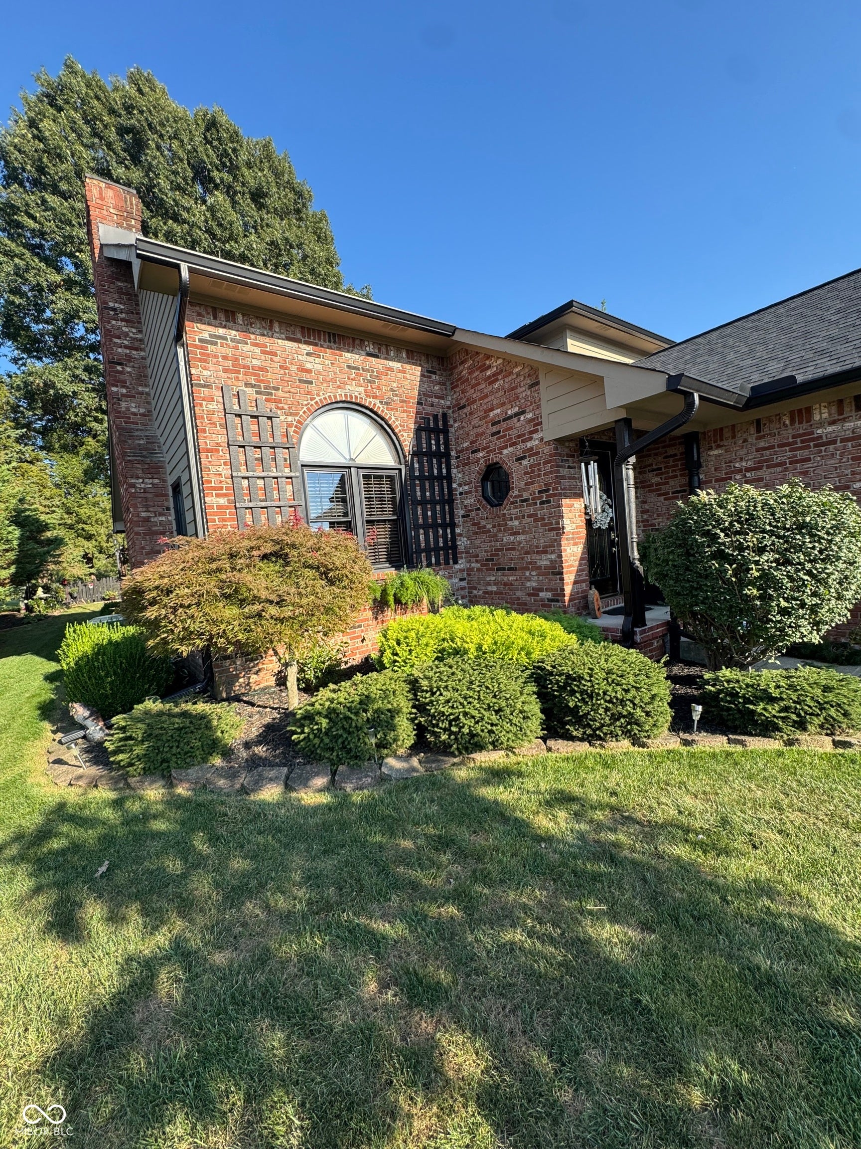 Brick exterior with arched entryway and black iron door accents, complemented by mature landscaping and manicured lawn