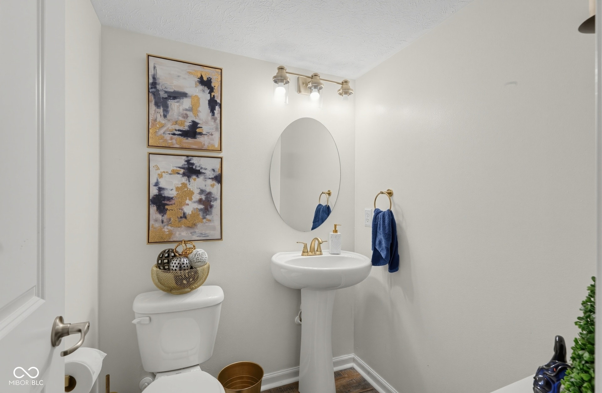 3394 S Bennett Drive, New Palestine, IN 46163 Main level half-Bath with pedestal sink, an oval mirror, gold-toned wall light fixture, and laminate-finish flooring