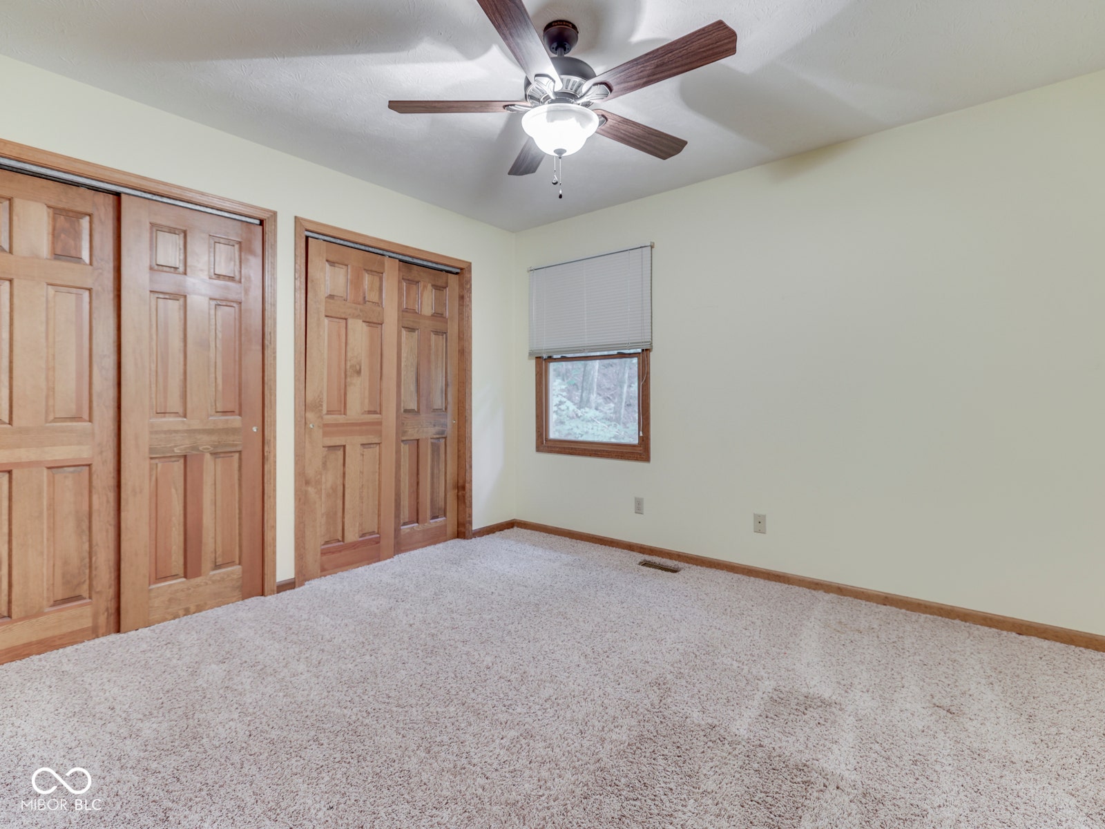 Plush carpeting, wood-finish sliding doors, ceiling fan with integrated lighting, and a single window with a roller shade