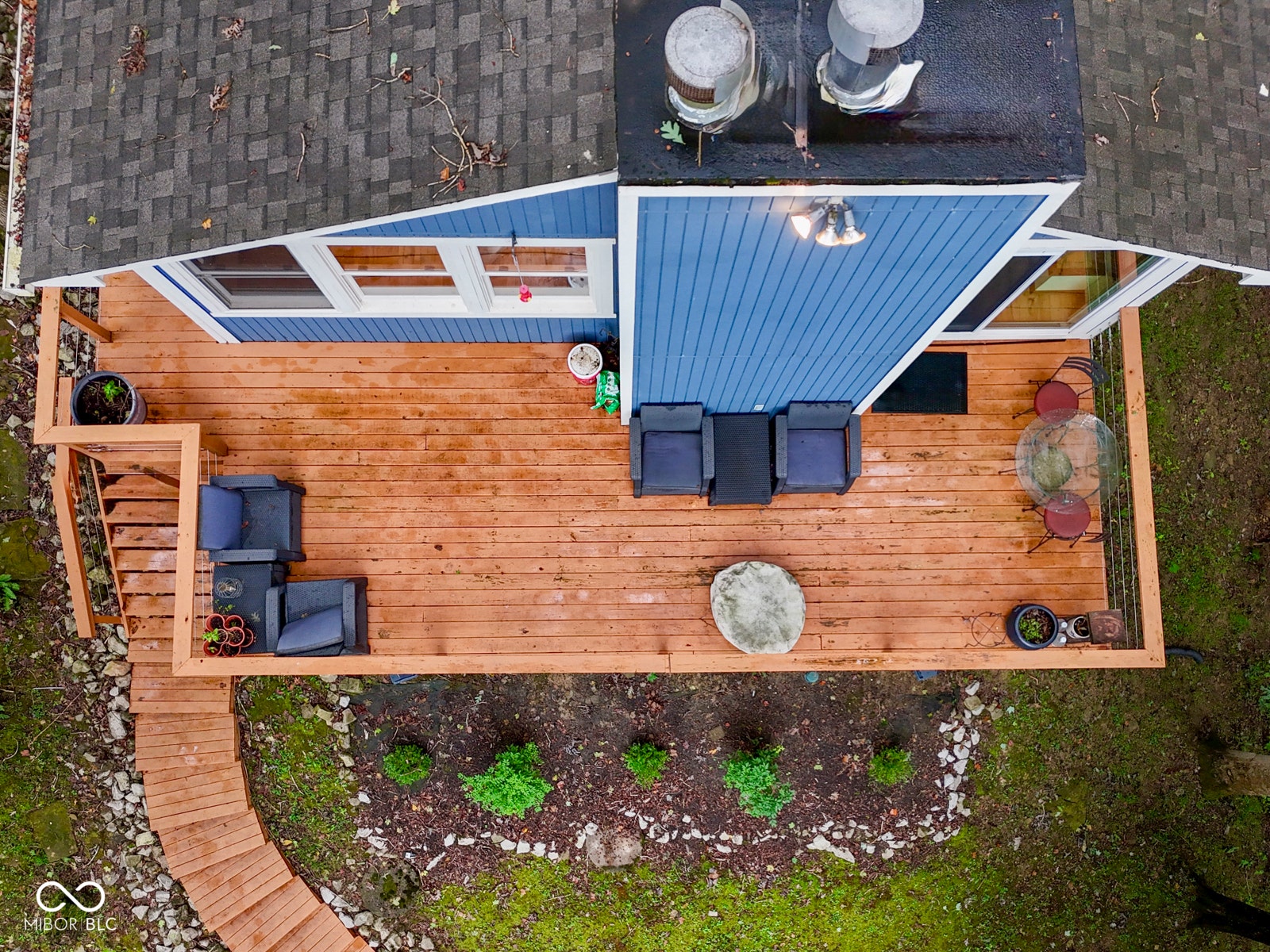 Expansive wood deck with stairs, blue siding, multiple windows, and exterior lighting