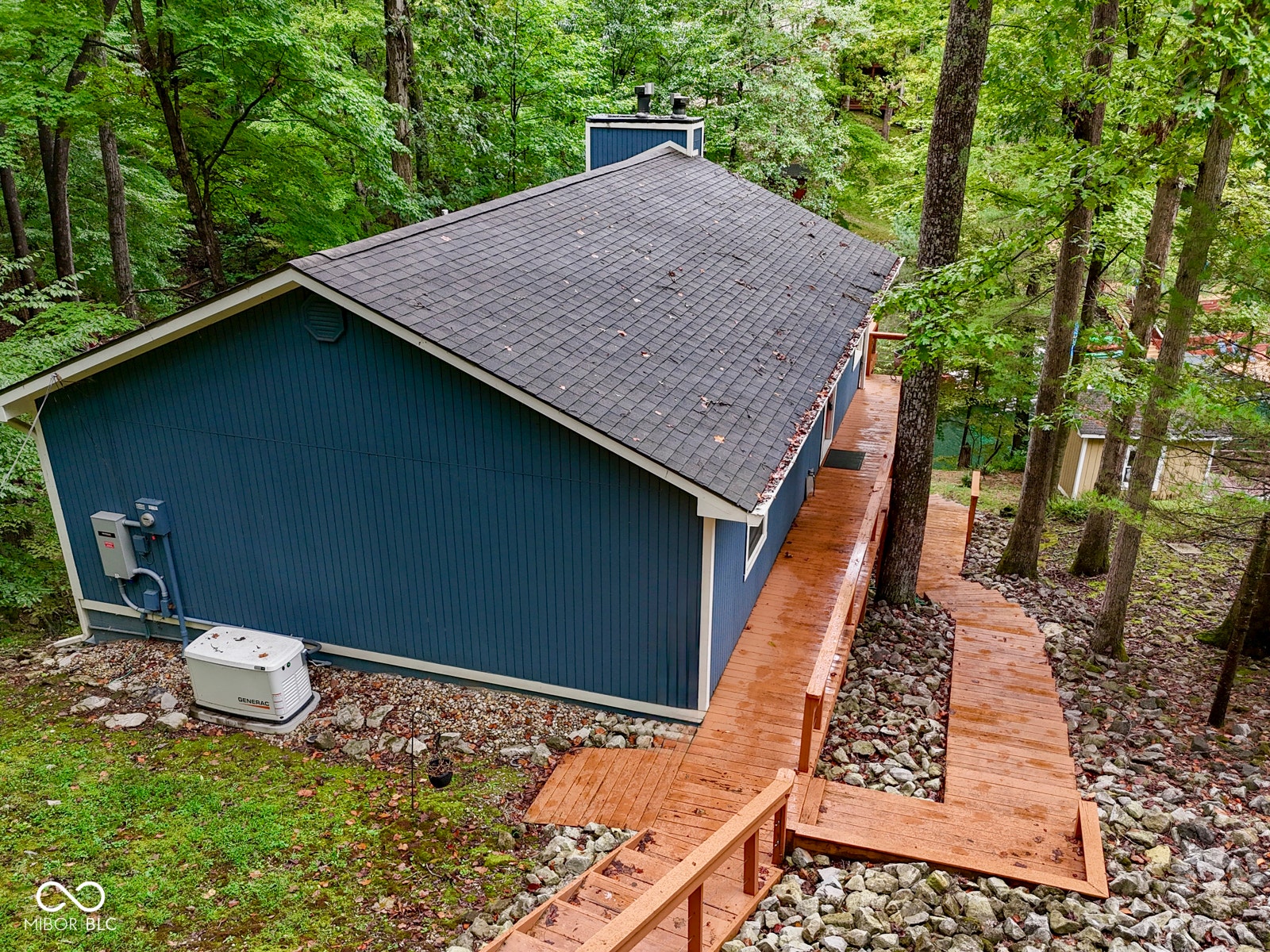 Deep blue siding exterior, dark shingle roof, extensive wood decking and stairs, and a visible whole-house generator