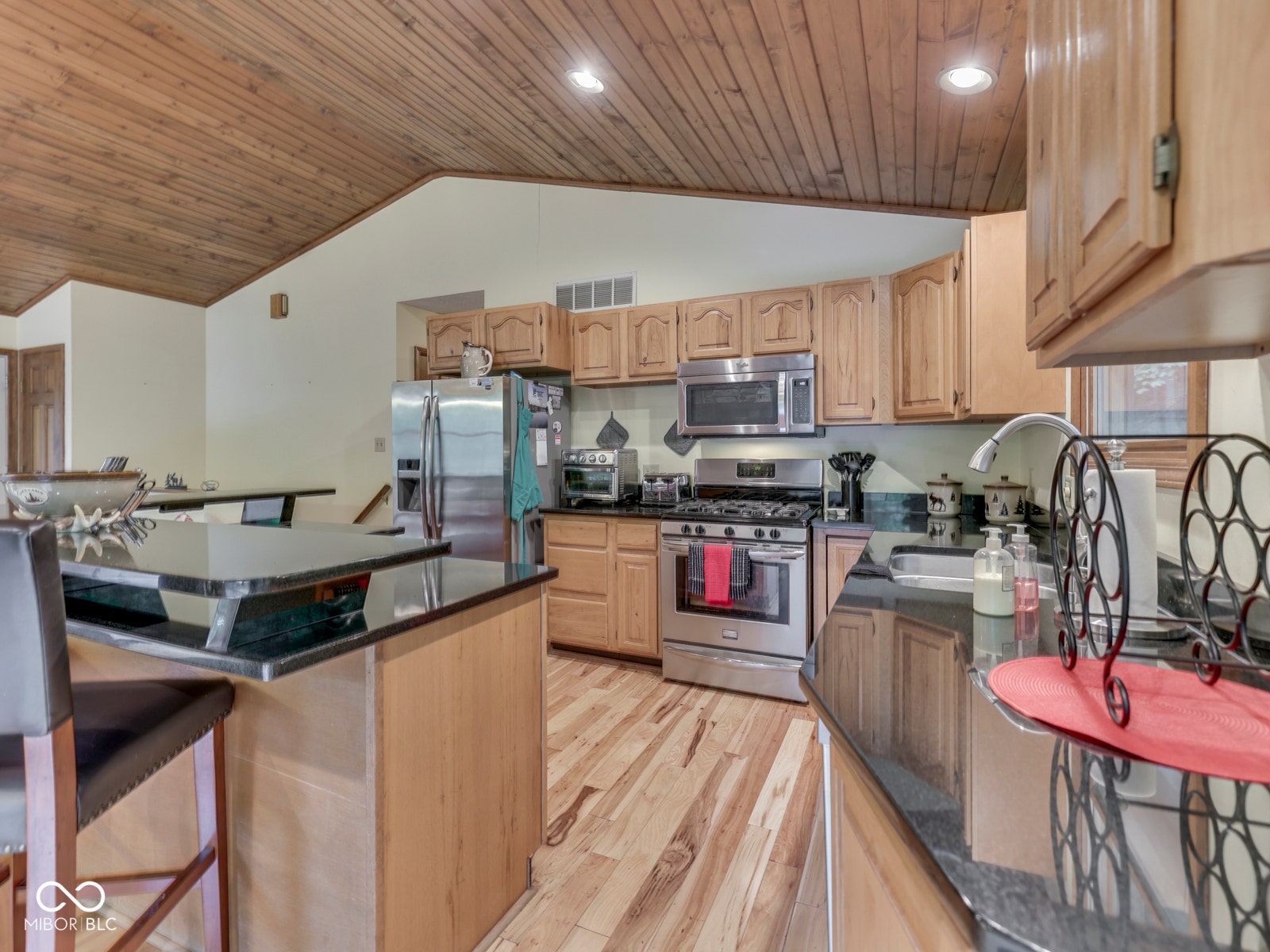 Kitchen featuring wood-finish flooring, natural wood cabinetry, stainless steel appliances, and dark countertops