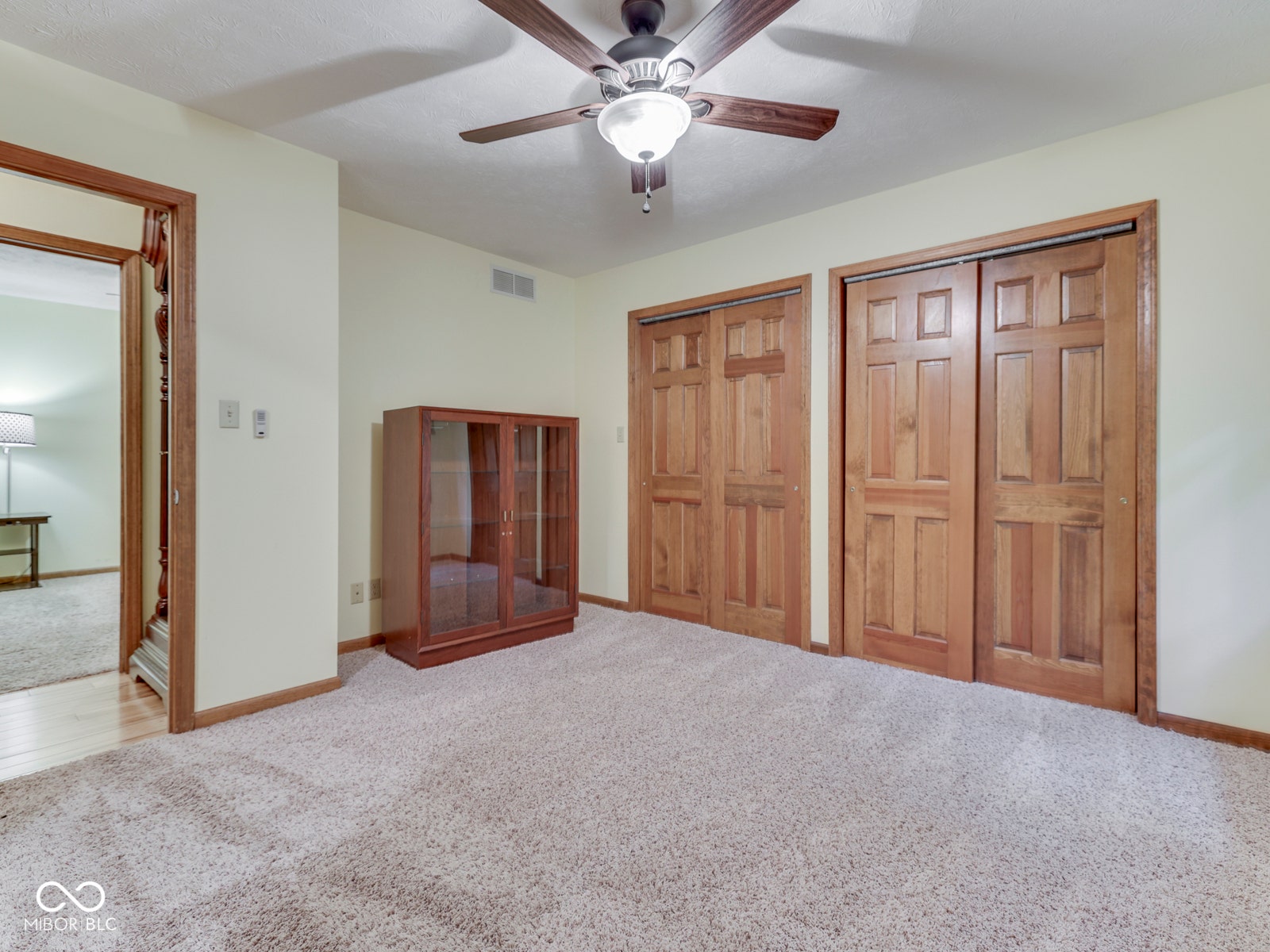 Textured carpeting, warm-toned wall paint, ceiling fan with integrated lighting, wood-finish bi-fold closet doors, and wood-trim doorway