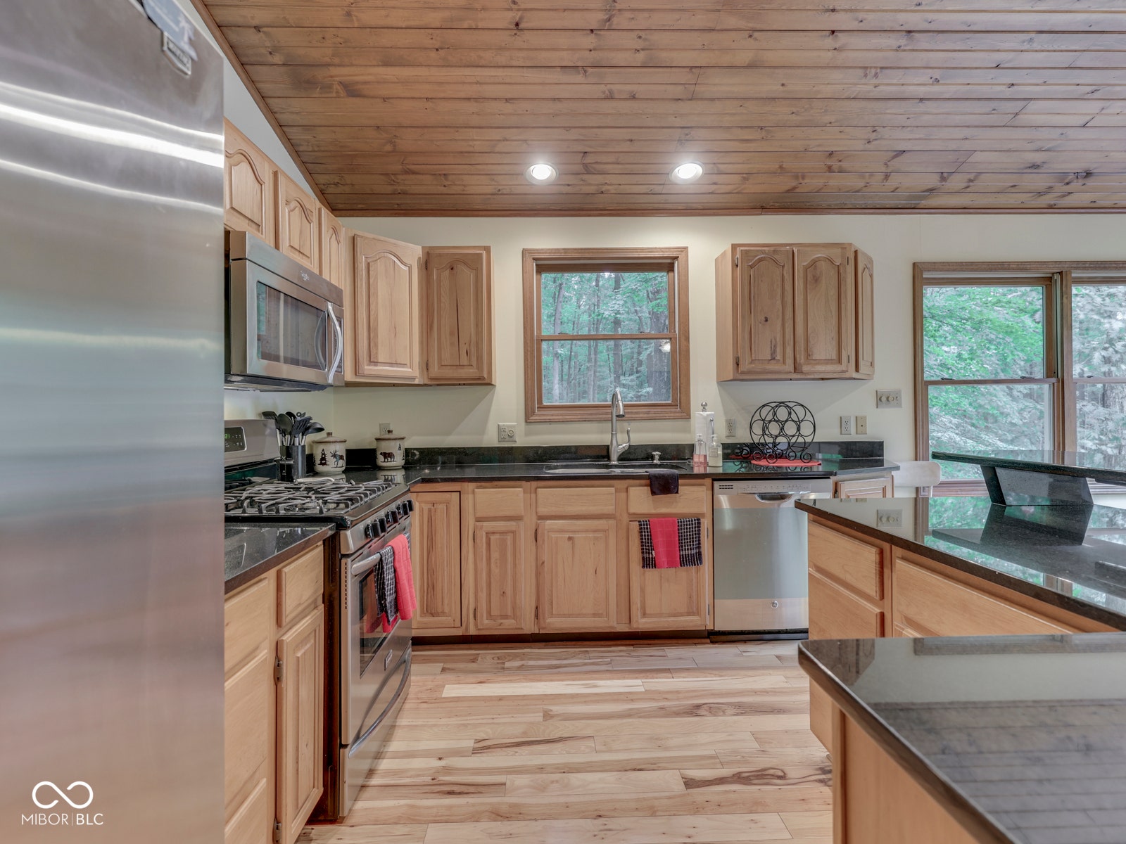 Kitchen featuring wood-finish flooring, natural wood cabinetry, black countertops, stainless steel appliances, and a wood-paneled ceiling