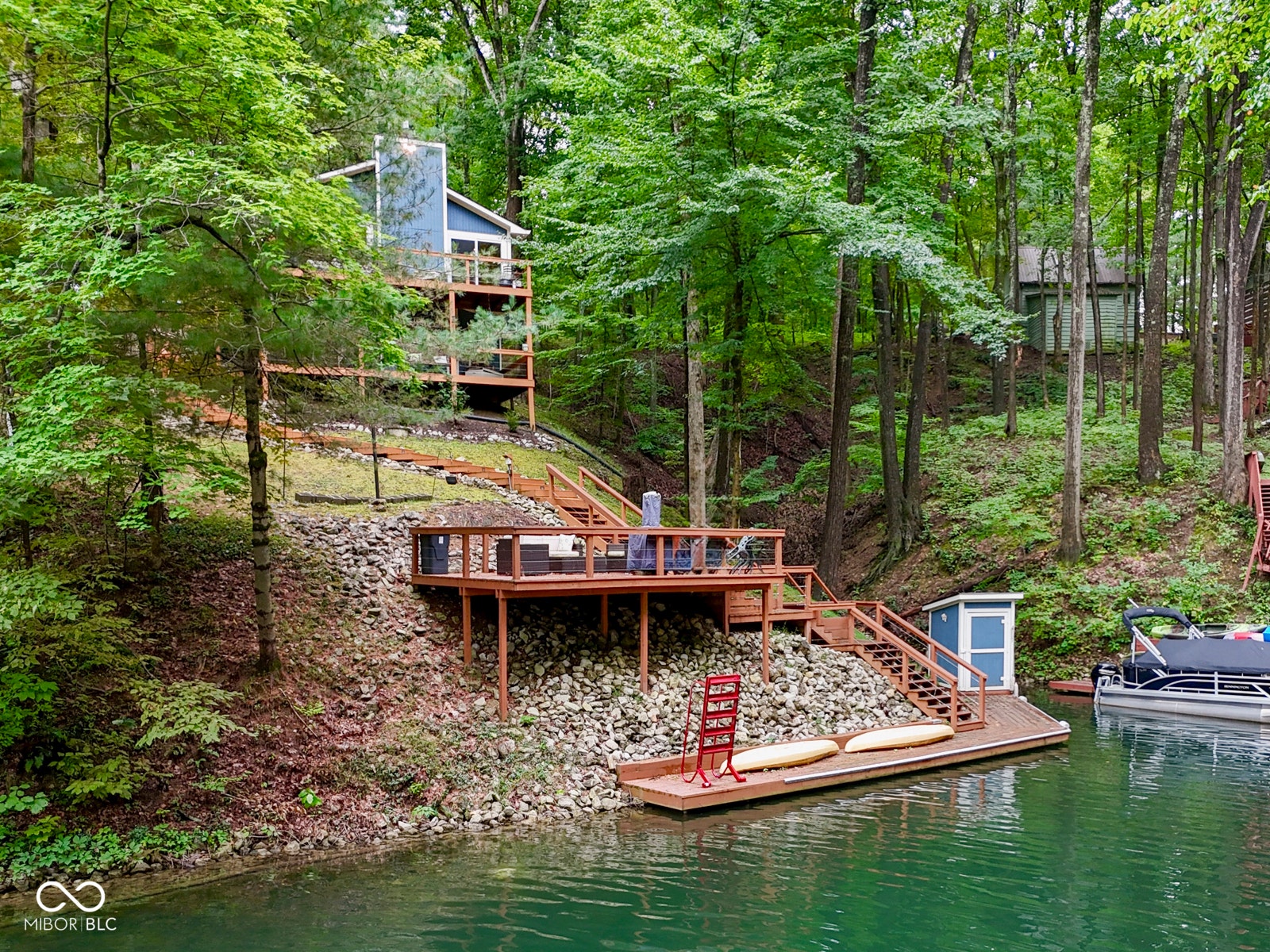Waterfront property featuring multiple tiered wood decks, a private dock with an attached storage shed, and direct water access