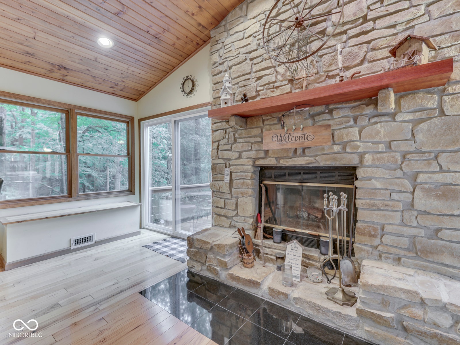 Vaulted wood-paneled ceiling, stone-clad fireplace with wood mantel, large windows, sliding glass door, and wood-finish flooring
