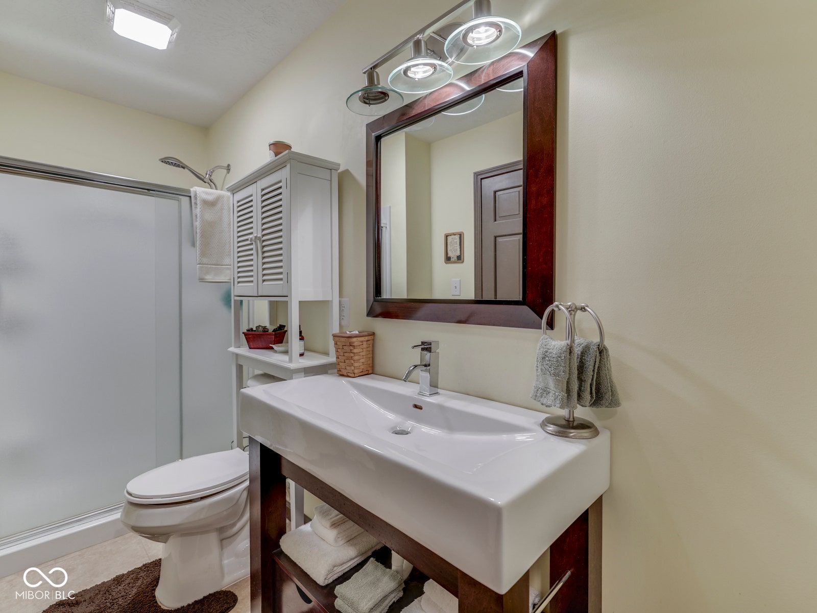 White rectangular vessel sink, dark wood-finish vanity, framed mirror, contemporary vanity lighting, and a shower with a frosted glass enclosure