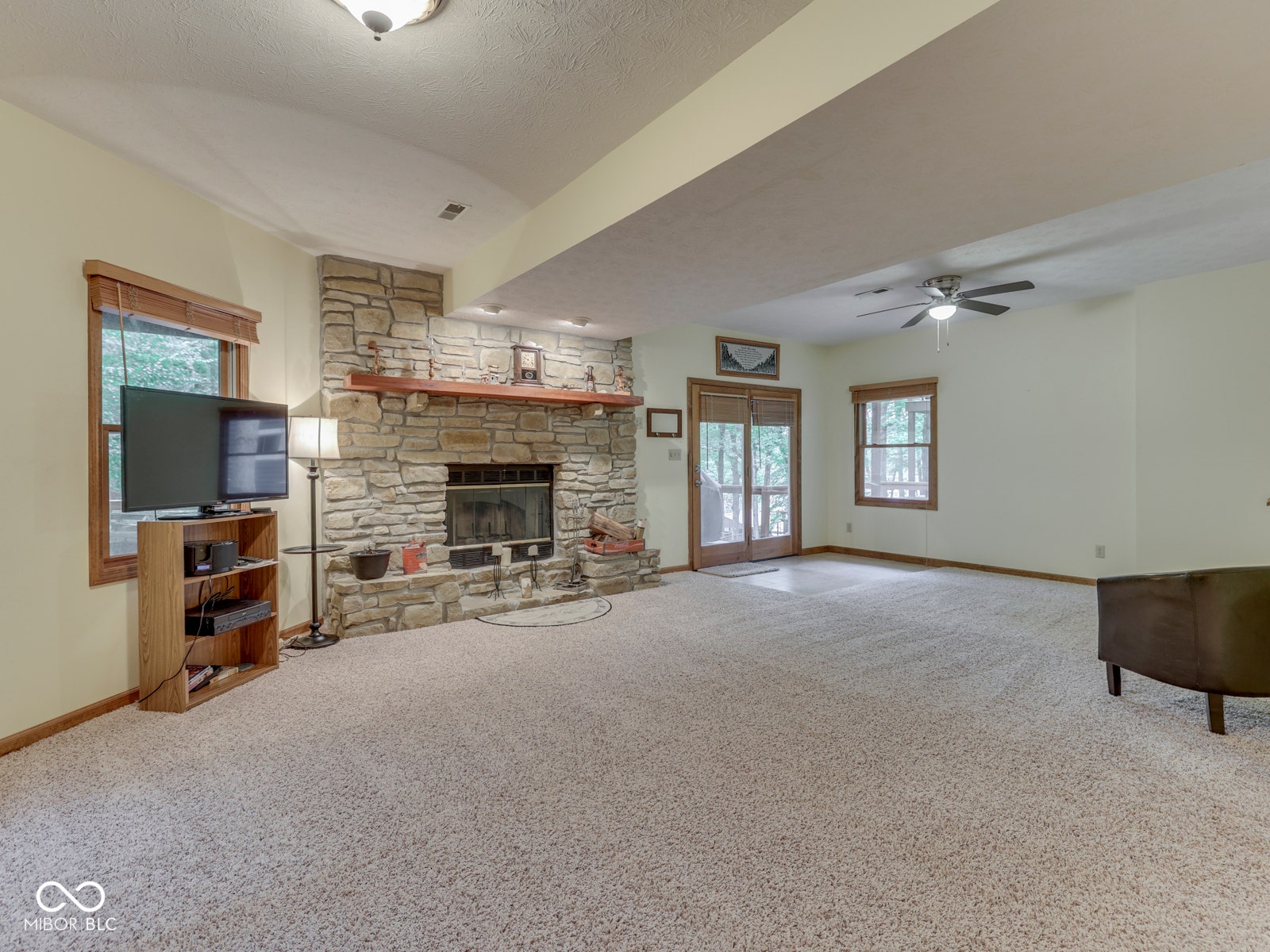 Stone fireplace with wood mantel, light-colored carpeting, recessed lighting, wood-framed windows, and a ceiling fan