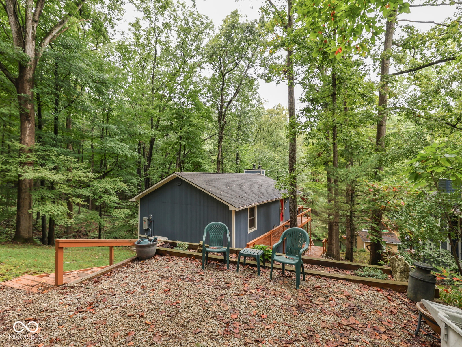 Exterior featuring a dark blue siding, red entry door, natural wood railing, and a gravel patio area