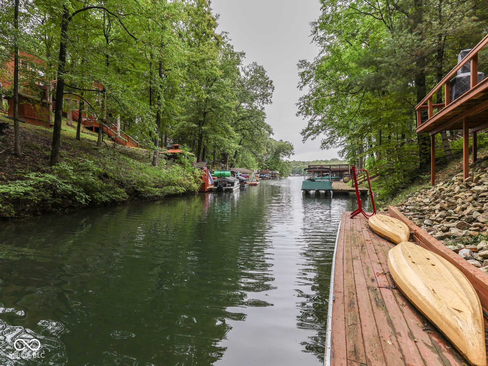 Waterfront property featuring a private wooden dock, lush mature trees, and sloped terrain with natural rock elements