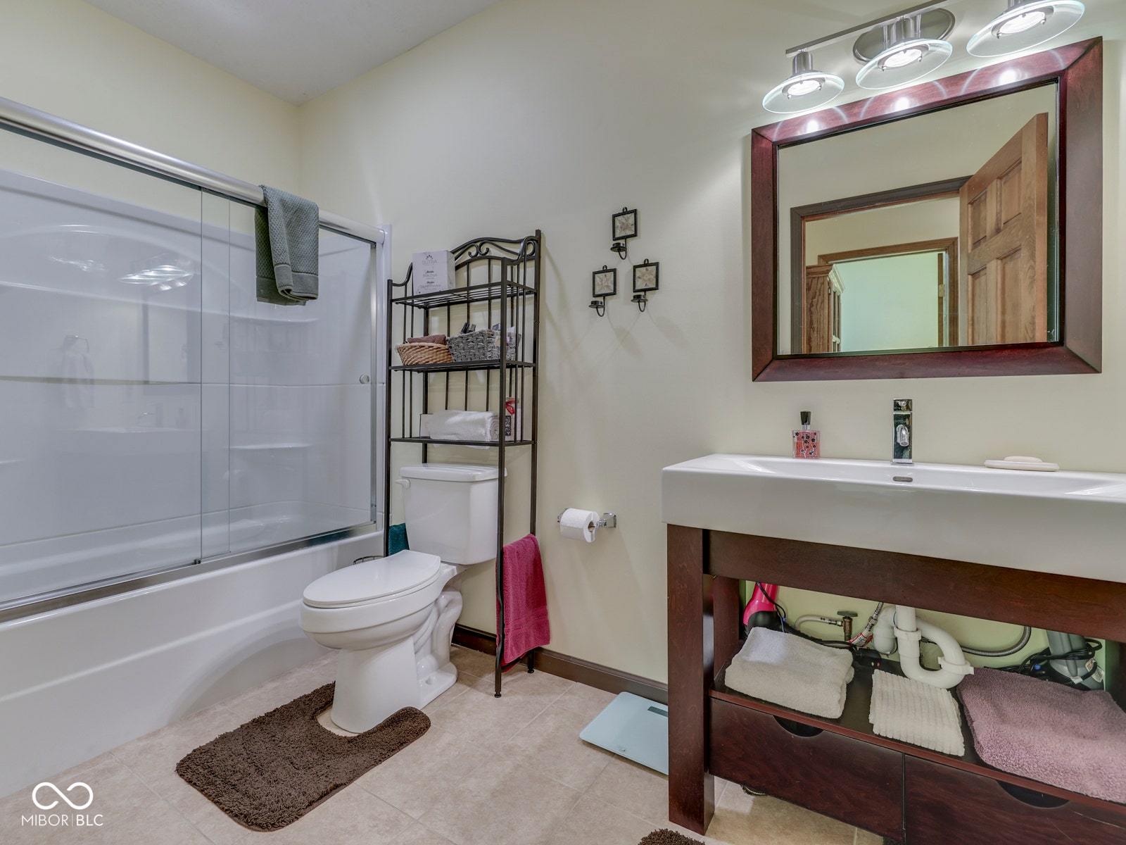 Bathroom featuring a tub with sliding glass doors, a vanity with an integrated sink, a framed mirror, and a three-light fixture