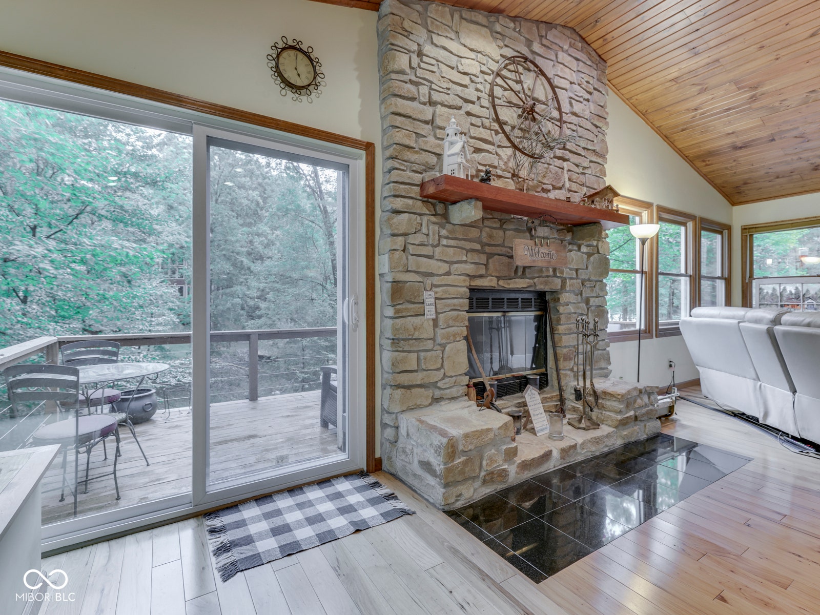 Stone-clad fireplace with hearth, wood-finish flooring, wood-paneled ceiling, and sliding glass doors to outdoor deck