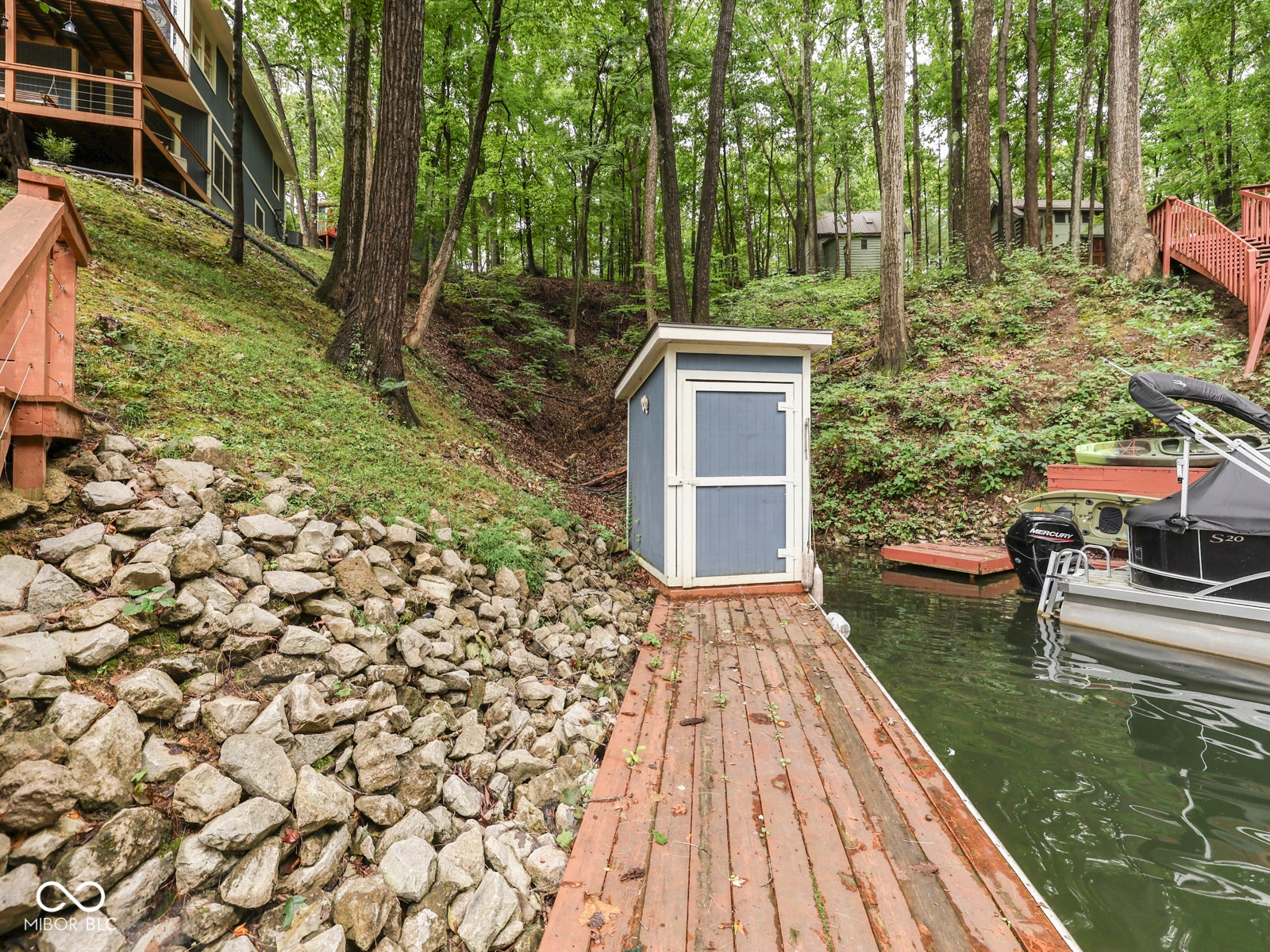 Waterfront property featuring a private wooden dock, a blue storage shed, and a stone retaining wall