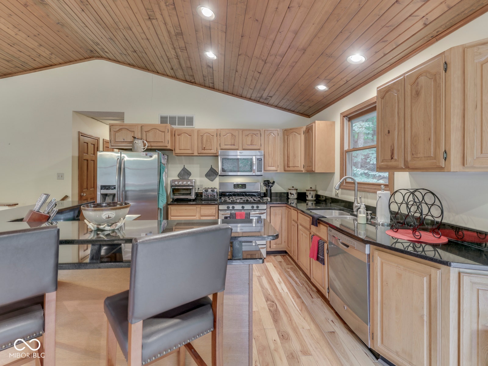 Kitchen featuring wood-finish flooring, vaulted wood-plank ceiling, black countertops, and stainless steel appliances