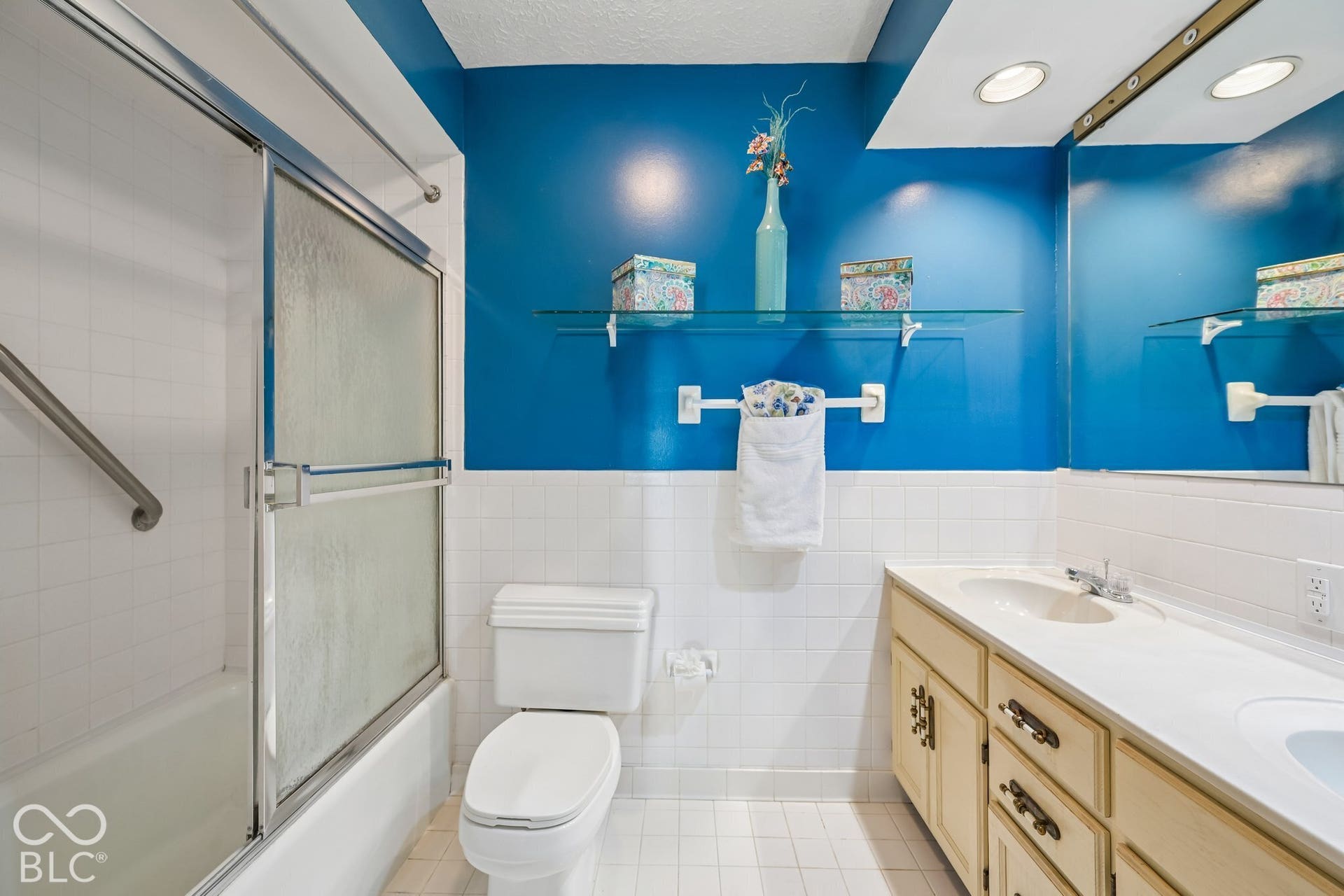 Bathroom featuring a shower-tub combination with sliding glass doors, white tile surround, and a grab bar