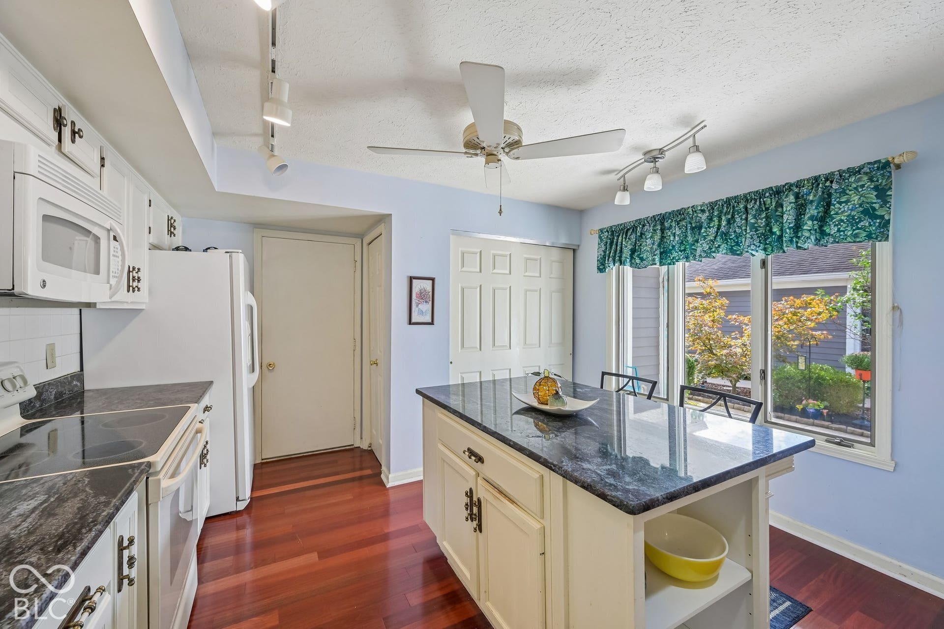 Kitchen featuring wood-finish flooring, white cabinetry, a central island with a dark countertop, and a window overlooking exterior landscaping