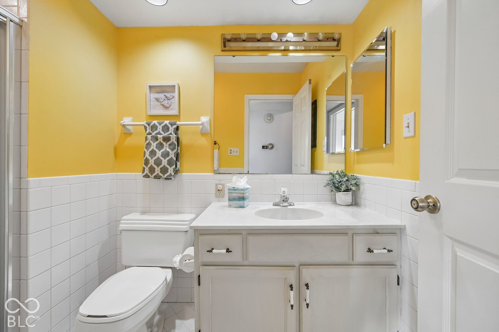 Bright and airy bathroom featuring soft yellow walls, white subway tile wainscoting, and recessed ceiling lighting
